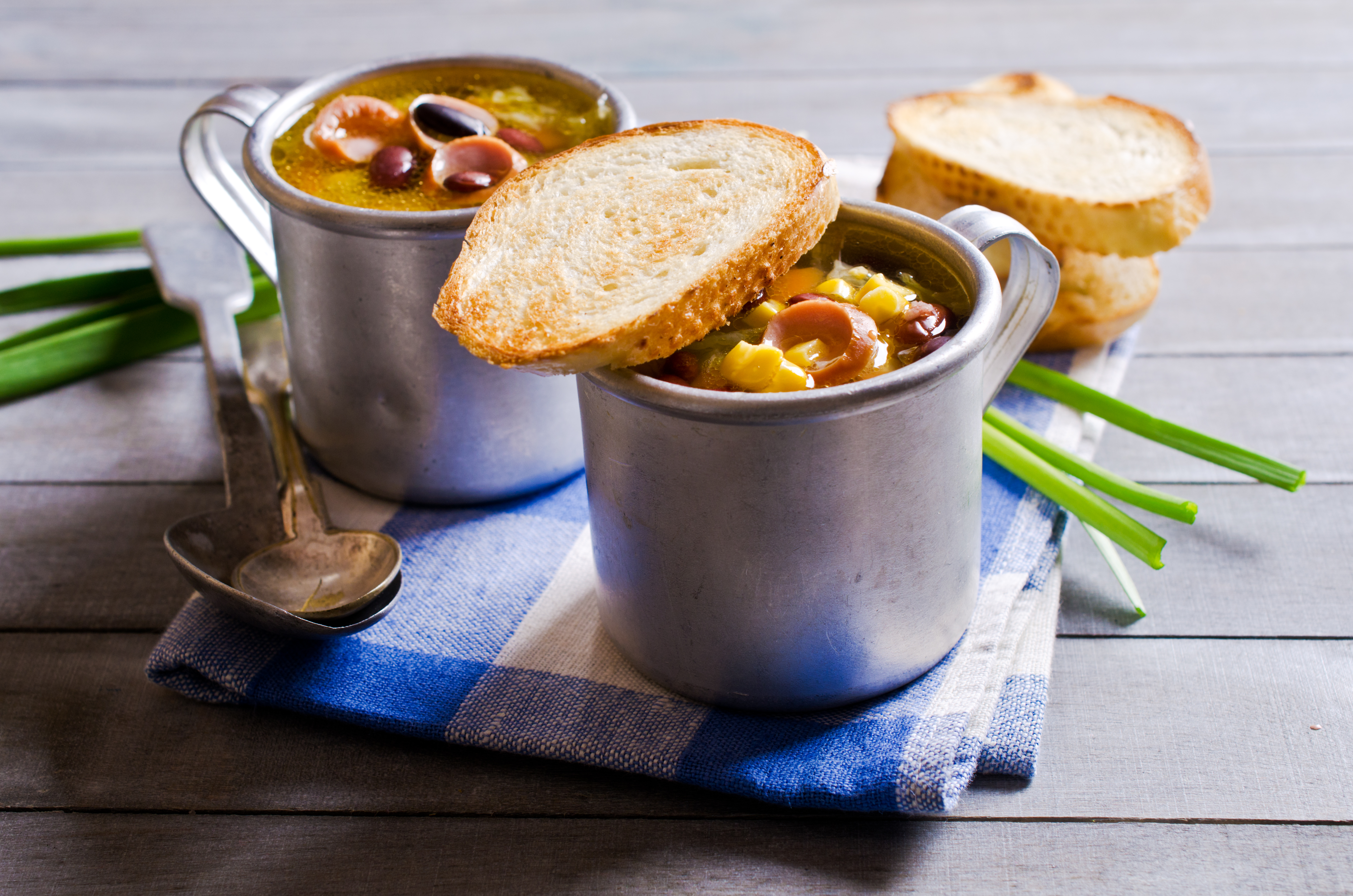 Soup with vegetables and sausages in a metallic plate on a wooden background. Selective focus.