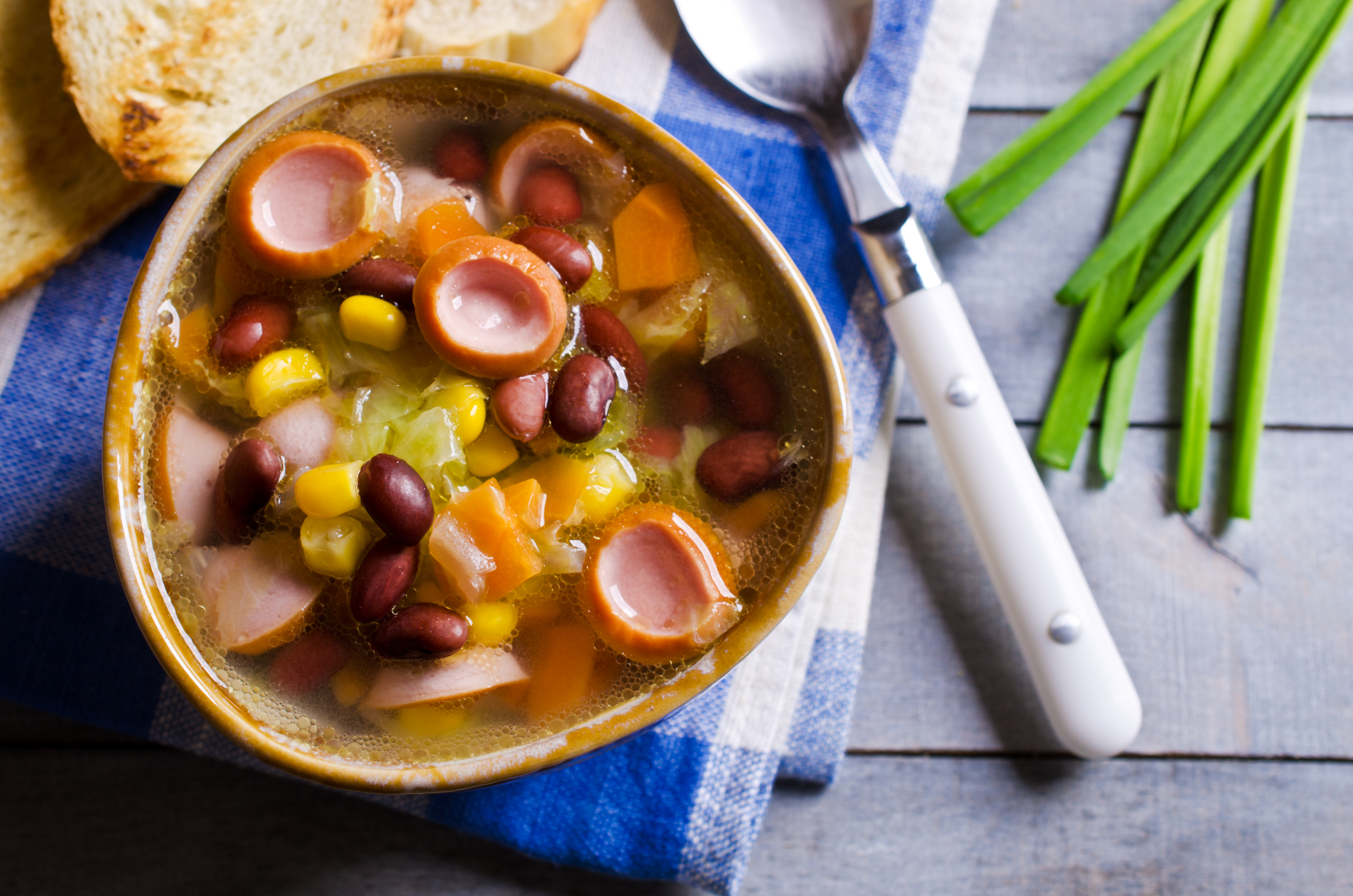 Soup with vegetables and sausages in a ceramic plate on a wooden background. Selective focus.