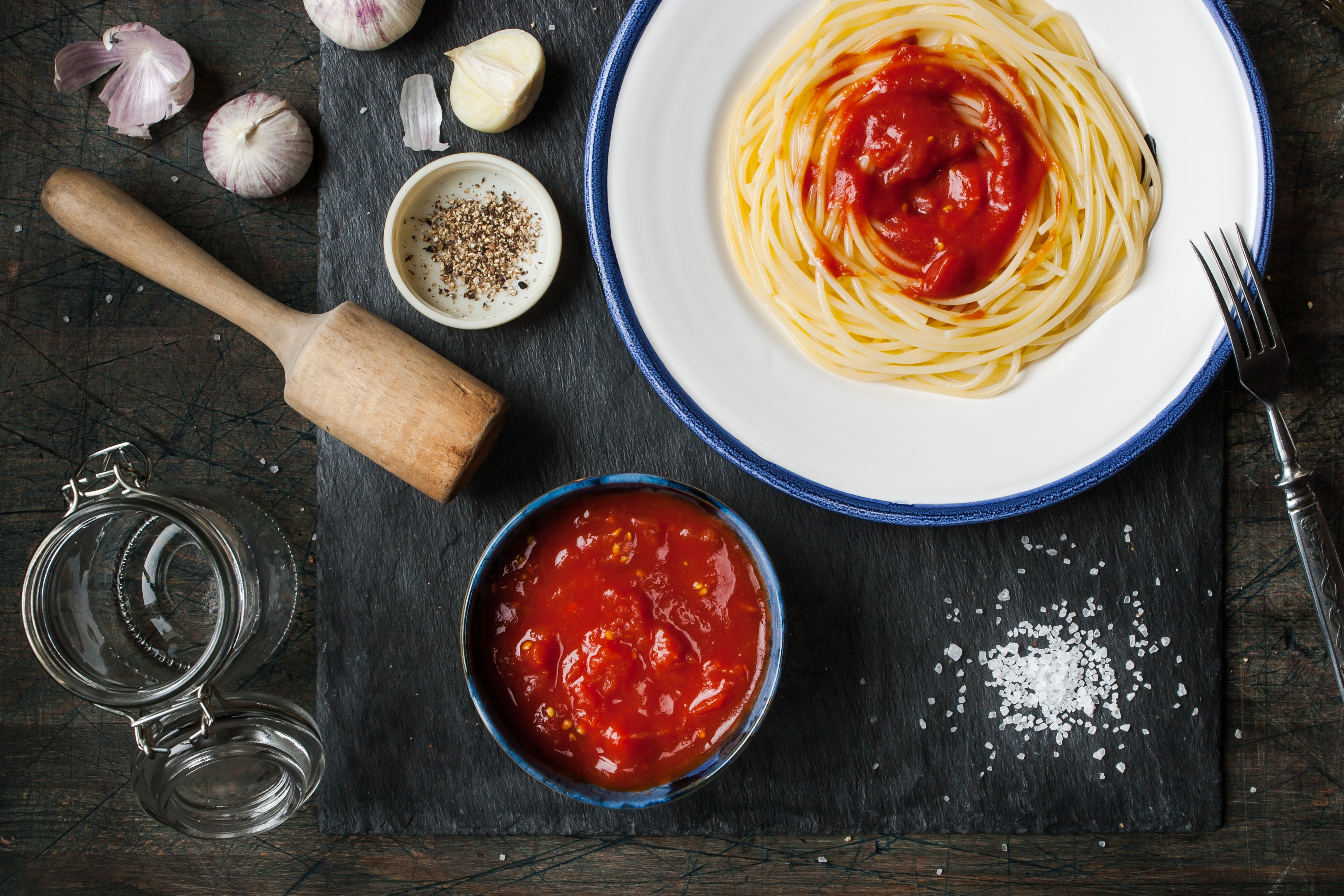Pureed tomatoes in a ceramic dish and a plate with spaghetti on a table horizontal