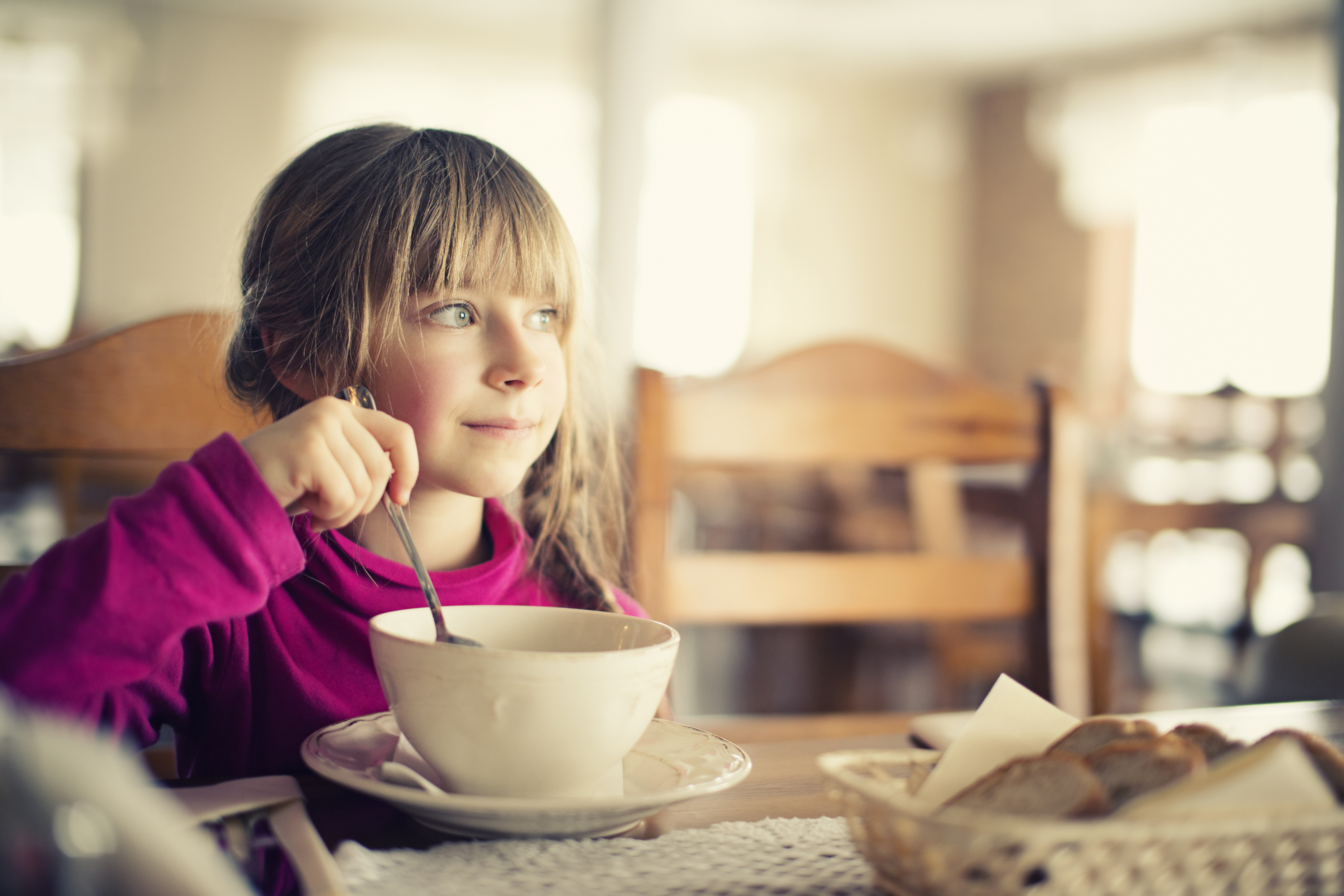 Beautiful smiling little girl eating a soup. Soft focus.