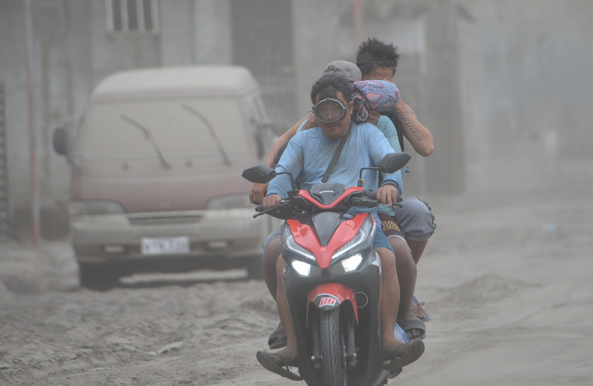 Residents riding on their motorcycle cover their faces as they traverse a road covered with ash, spewed by Taal volcano in Agoncillo town, Batangas province south of Manila on January 15, 2020. - Taal volcano in the Philippines could spew lava and ash for weeks, authorities warned on January 14, leaving thousands in limbo after fleeing their homes fearing a massive eruption. (Photo by Ted ALJIBE / AFP)