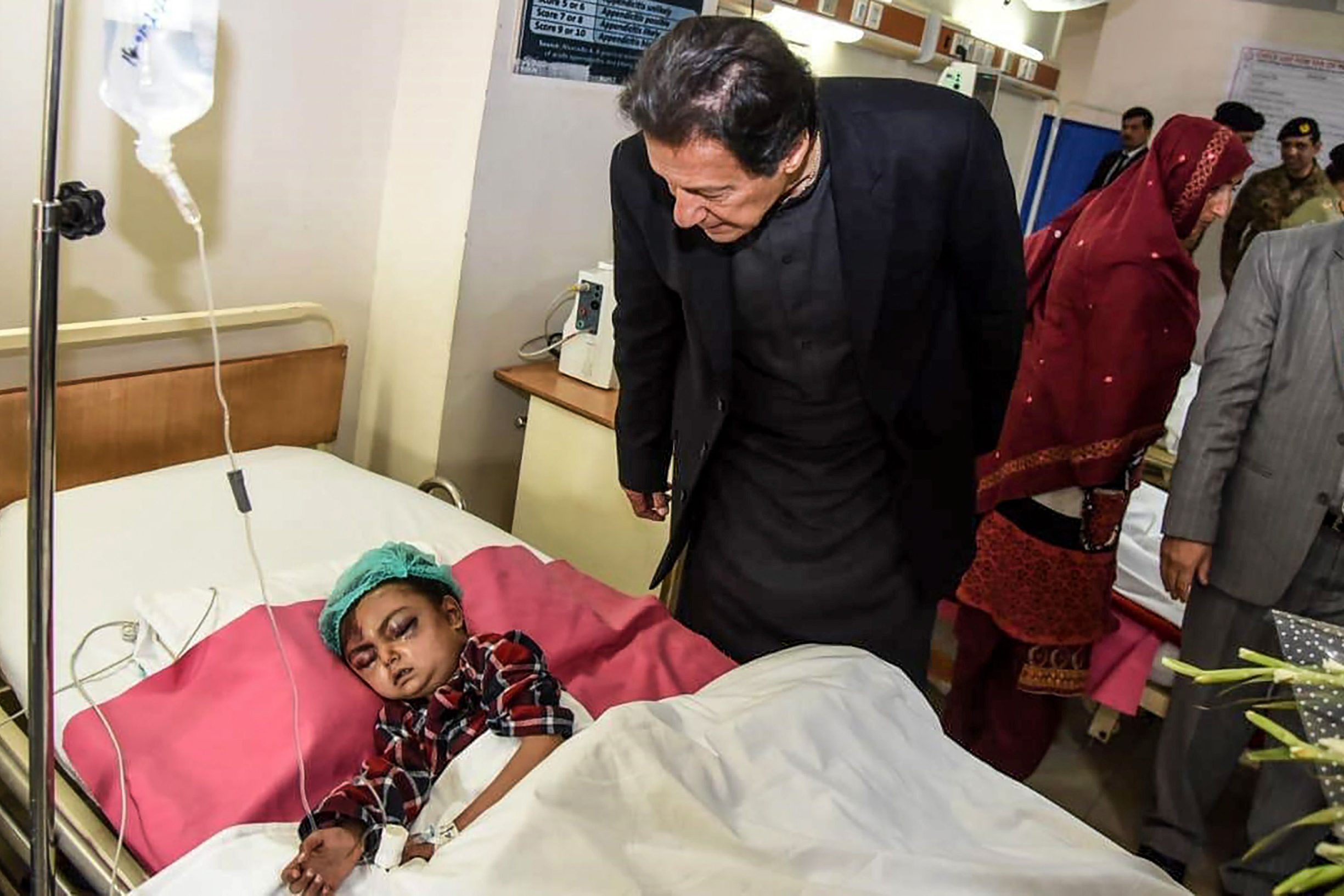 In this handout photograph taken and released by the Pakistan Press Information Department (PID) on January 15, 2020, Pakistan's Prime Minister Imran Khan (C) looks at a young injured avalanche victim at a military hospital in Muzaffarabad, the capital of Pakistan-administered Kashmir. - Avalanches, flooding and harsh winter weather killed more than 130 people across Pakistan and Afghanistan in recent days, leaving others stranded by heavy snowfall, officials said on January 14. (Photo by Handout / PID / AFP) / RESTRICTED TO EDITORIAL USE - MANDATORY CREDIT 