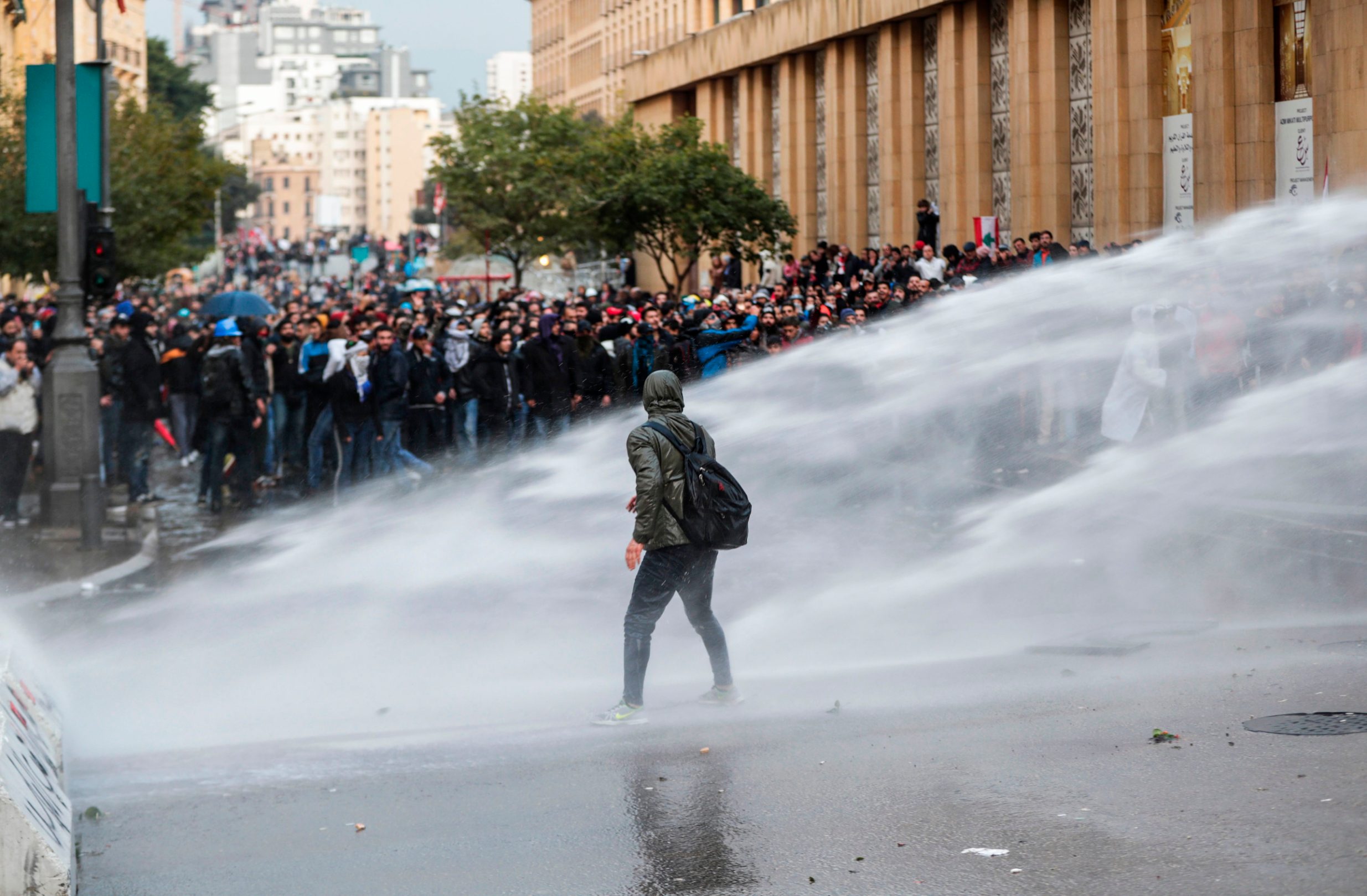 An anti-government protester walks through water cannon spray from security forces during clashes in the central downtown district of the Lebanese capital near the parliament headquarters on January 18, 2020. (Photo by ANWAR AMRO / AFP)