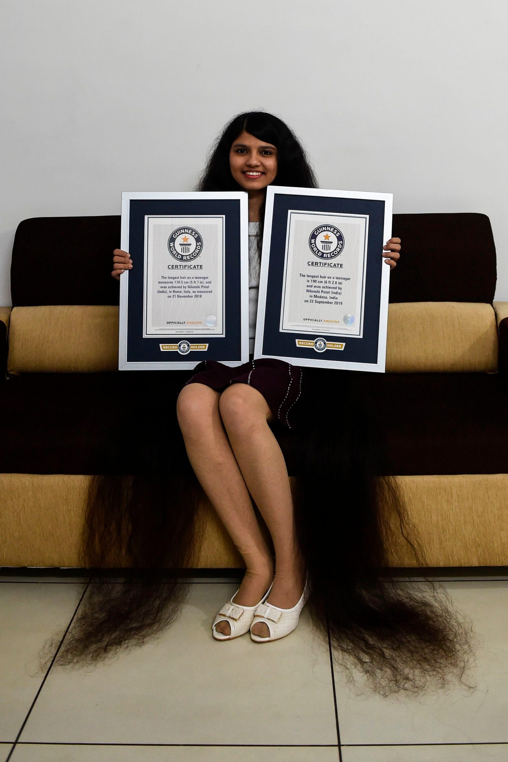Nilanshi Patel, 17, poses for picture with the 2018 (L) and 2019 Guinness World Record certificates for the longest hair in the teenager category, at Modasa town, some 110 Kms from Ahmedabad on January 19, 2020. - Patel has been awarded the 2019 Guinness World Record for the longest hair at 190 cm in the teenager category. In 2018 she bagged Guinness World Record in the same category at 170,5 cm. (Photo by SAM PANTHAKY / AFP)