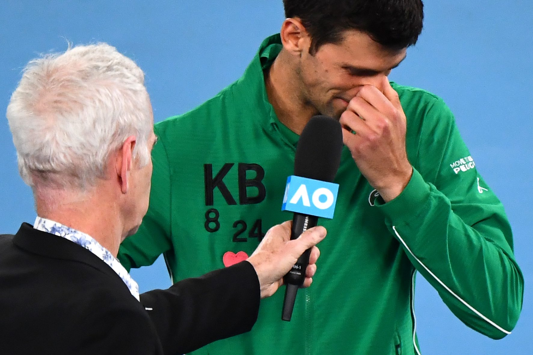 Serbia's Novak Djokovic gets emotional as he talks about Kobe Bryant next to former US tennis player John McEnroe after winning the men's singles quarter-final match against Canada's Milos Raonic on day nine of the Australian Open tennis tournament in Melbourne on January 28, 2020. (Photo by William WEST / AFP) / IMAGE RESTRICTED TO EDITORIAL USE - STRICTLY NO COMMERCIAL USE