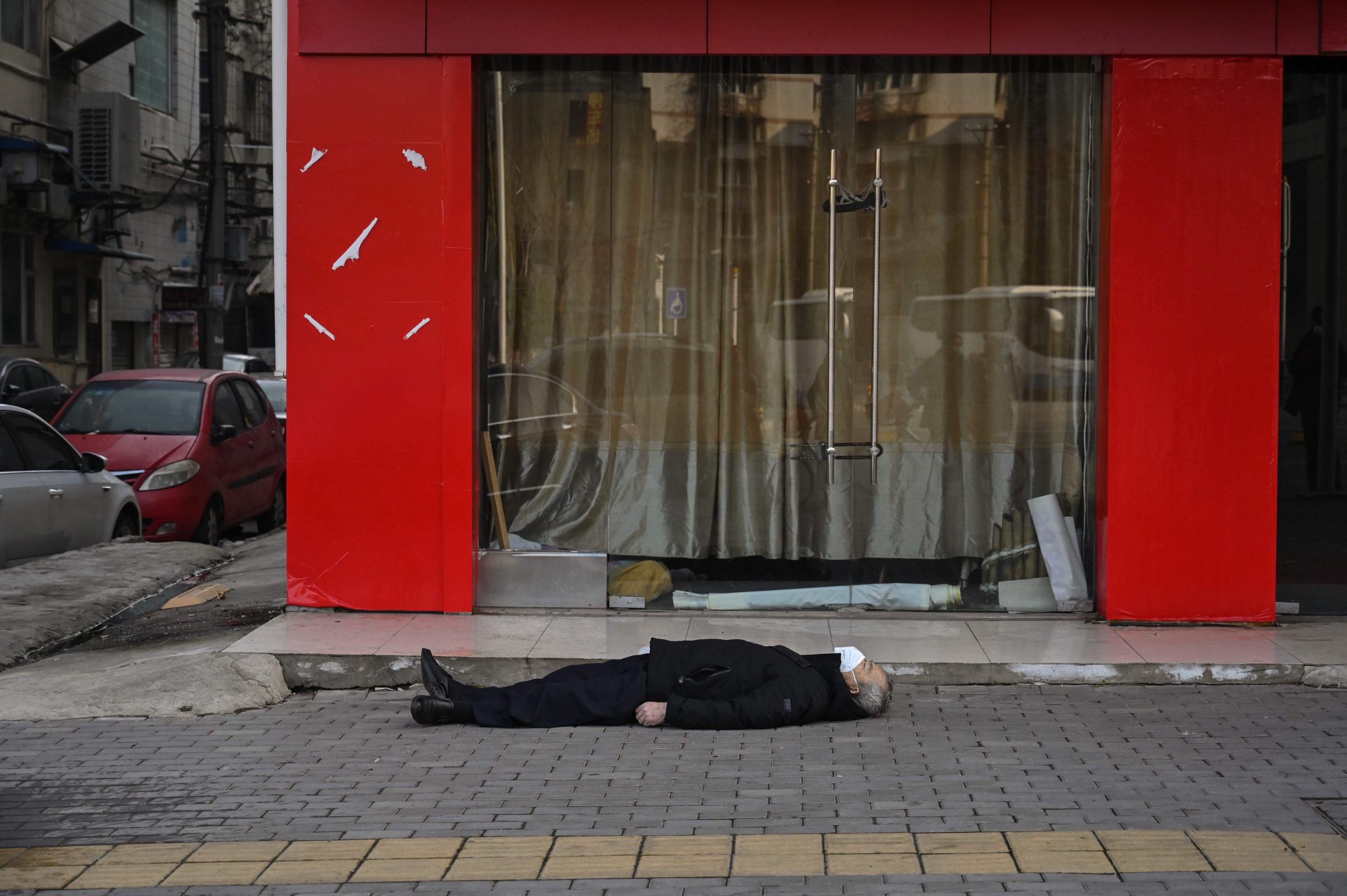 This photo taken on January 30, 2020 shows an elderly man wearing a facemask lying on the pavement after he collapsed and died along a street near a hospital in Wuhan. - AFP journalists saw the body on January 30, not long before an emergency vehicle arrived carrying police and medical staff in full-body protective suits. The World Health Organization declared a global emergency over the new coronavirus, as China reported on January 31 the death toll had climbed to 213 with nearly 10,000 infections. (Photo by Hector RETAMAL / AFP) / TO GO WITH China-health-virus-death,SCENE by Leo RAMIREZ and Sebastien RICCI