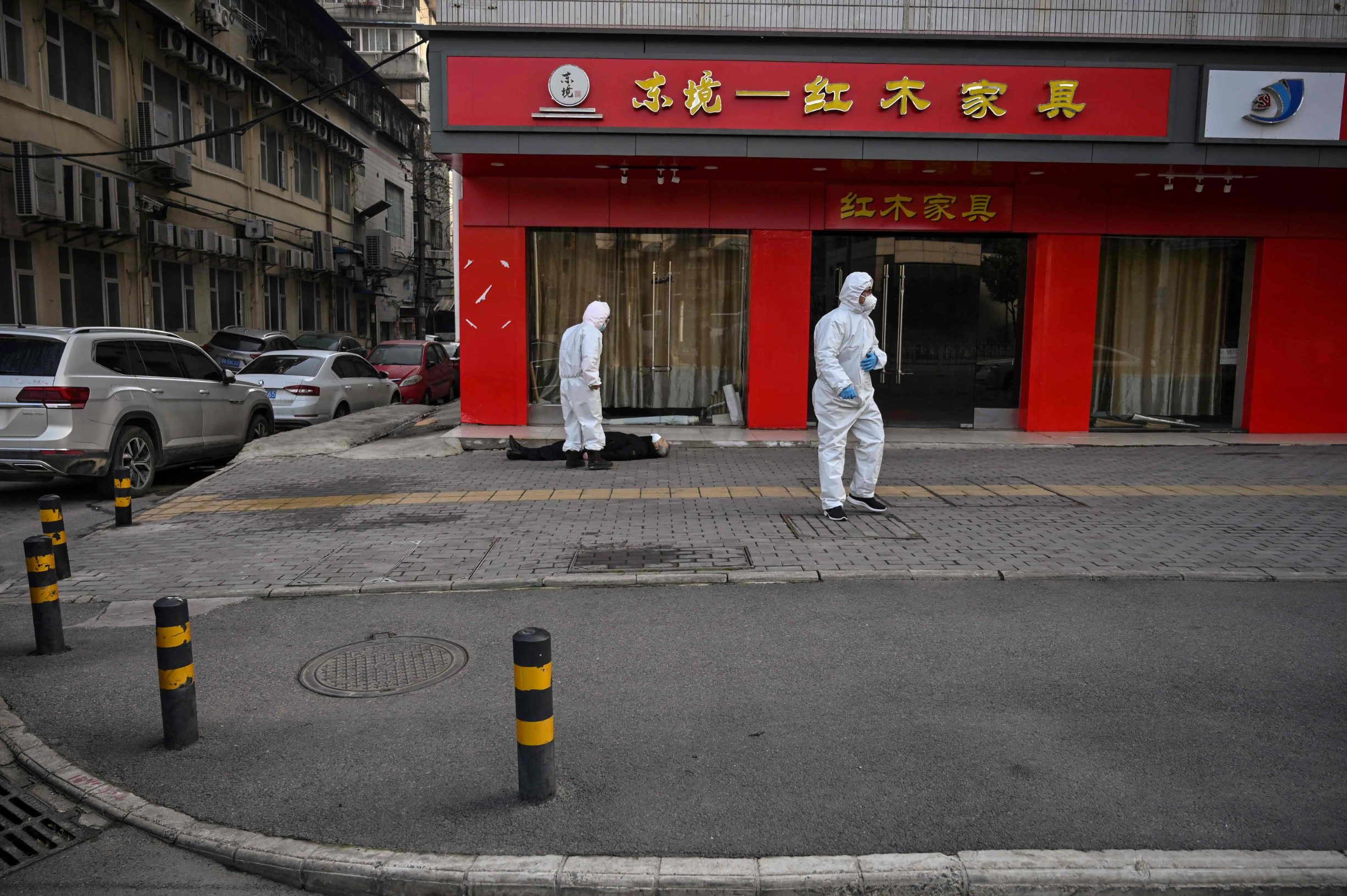 This photo taken on January 30, 2020 shows officials in protective suits checking on an elderly man wearing a facemask who collapsed and died on a street near a hospital in Wuhan. - AFP journalists saw the body on January 30, not long before an emergency vehicle arrived carrying police and medical staff in full-body protective suits. The World Health Organization declared a global emergency over the new coronavirus, as China reported on January 31 the death toll had climbed to 213 with nearly 10,000 infections. (Photo by Hector RETAMAL / AFP) / TO GO WITH China-health-virus-death,SCENE by Leo RAMIREZ and Sebastien RICCI