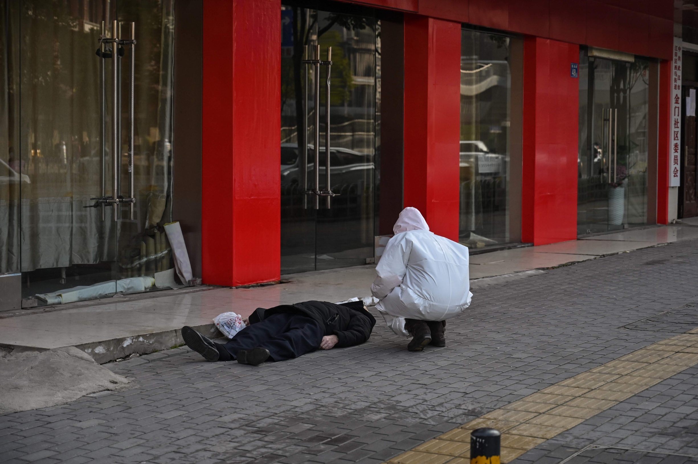 This photo taken on January 30, 2020 shows an official in a protective suit checking on an elderly man wearing a facemask who collapsed and died on a street near a hospital in Wuhan. - AFP journalists saw the body on January 30, not long before an emergency vehicle arrived carrying police and medical staff in full-body protective suits. The World Health Organization declared a global emergency over the new coronavirus, as China reported on January 31 the death toll had climbed to 213 with nearly 10,000 infections. (Photo by Hector RETAMAL / AFP) / TO GO WITH China-health-virus-death,SCENE by Leo RAMIREZ and Sebastien RICCI