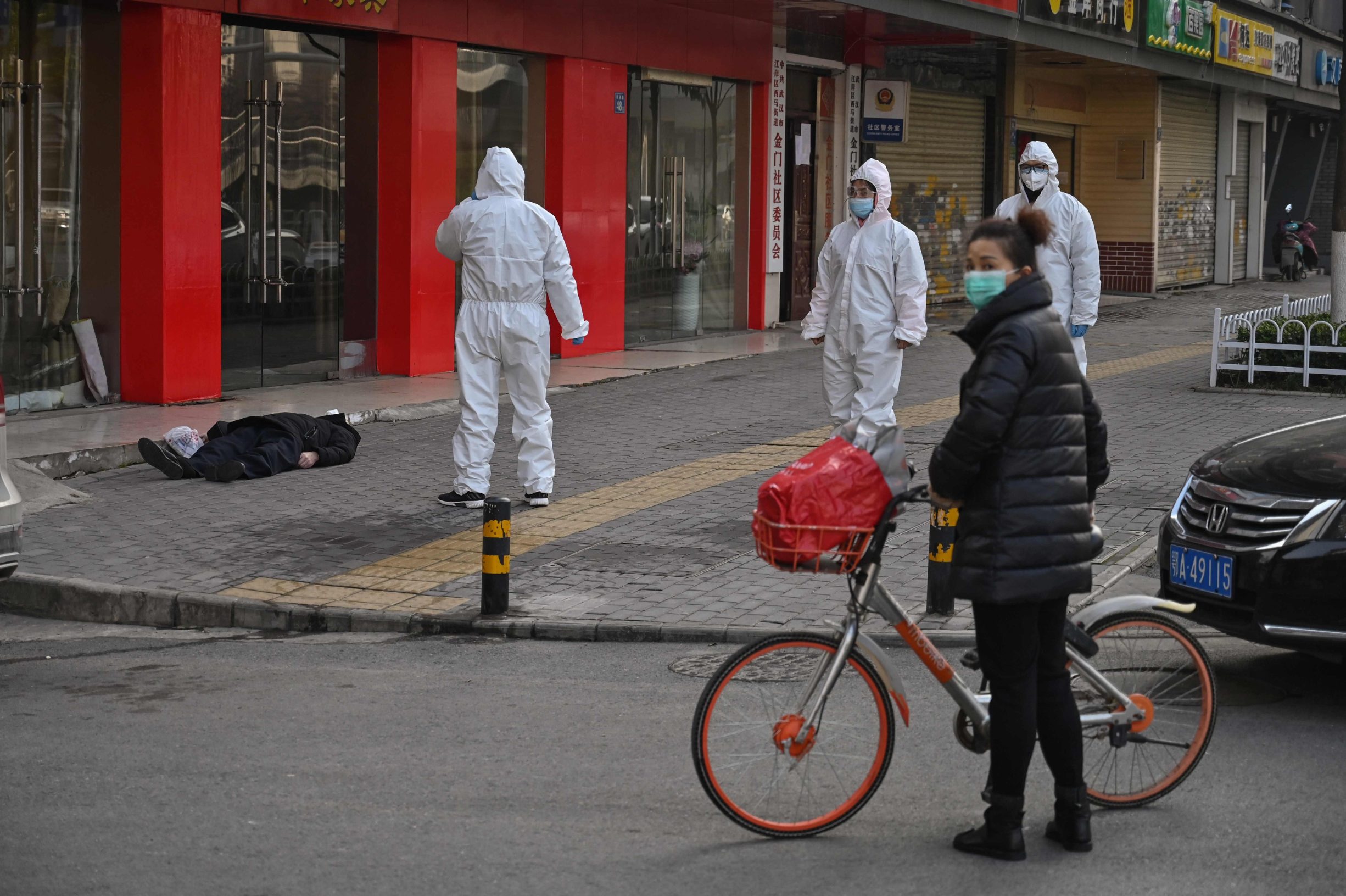 This photo taken on January 30, 2020 shows officials in protective suits checking on an elderly man wearing a facemask who collapsed and died on a street near a hospital in Wuhan. - AFP journalists saw the body on January 30, not long before an emergency vehicle arrived carrying police and medical staff in full-body protective suits. The World Health Organization declared a global emergency over the new coronavirus, as China reported on January 31 the death toll had climbed to 213 with nearly 10,000 infections. (Photo by Hector RETAMAL / AFP) / TO GO WITH China-health-virus-death,SCENE by Leo RAMIREZ and Sebastien RICCI