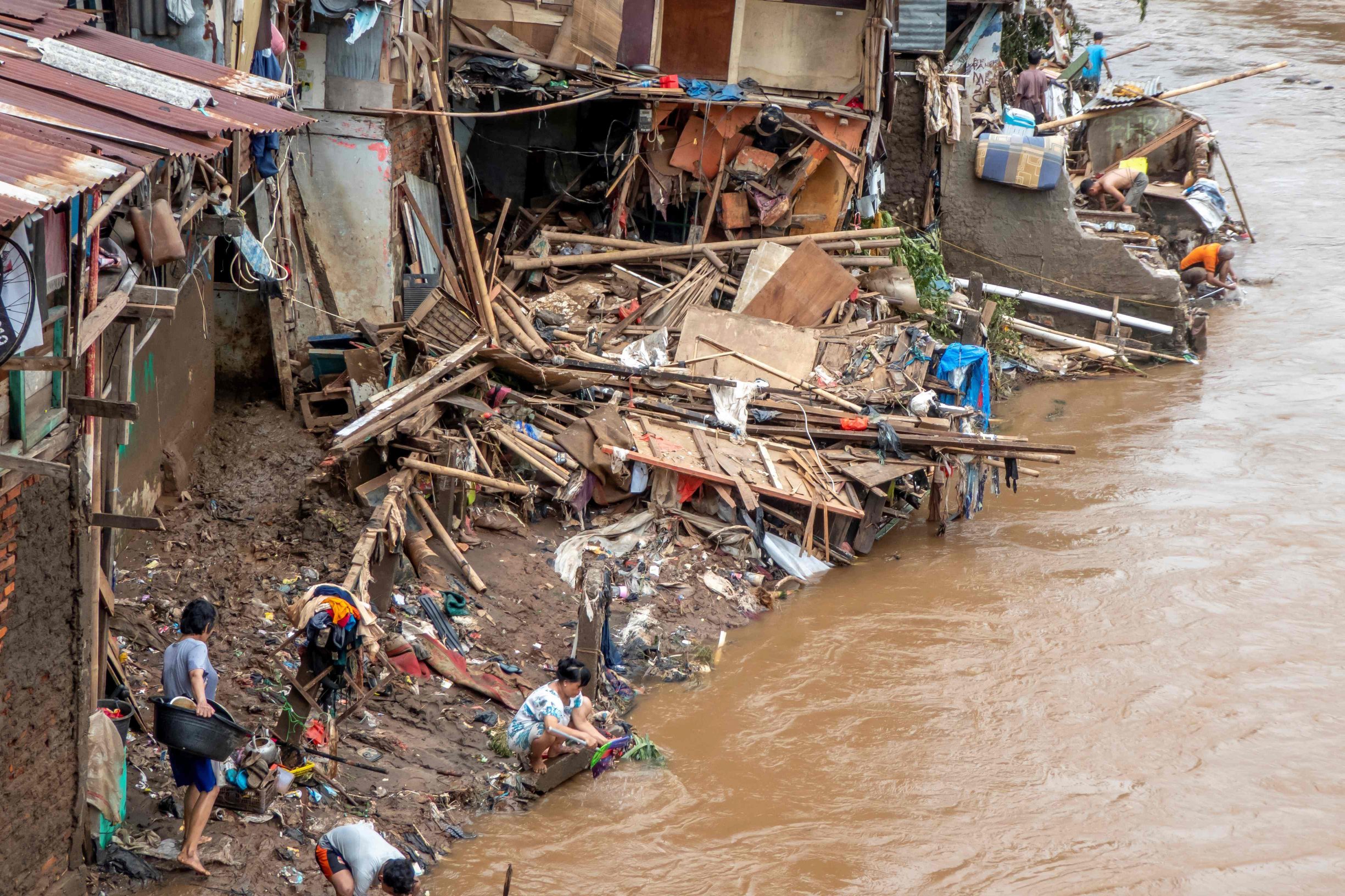 Indonesians clean their homes and cutlery along the river in Jakarta on January 3, 2020, after flooding triggered by heavy rain which started on New Year's Eve hit the area. - Indonesian rescuers mounted a desperate search on January 3 for those missing after flash floods and landslides sparked by torrential rains killed at least 43 people across the Jakarta region, leaving whole districts under water and thousands homeless. (Photo by BAY ISMOYO / AFP)