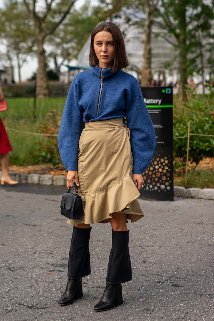 NEW YORK, NY - SEPTEMBER 09: A guest wearing a blue quarter-zip pullover, khaki wrap skirt, and black knee-high boots attends the Carolina Herrera show during New York Fashion Week at the Garden of the Battery on September 9, 2019 in New York City. (Photo by David Dee Delgado/Getty Images)