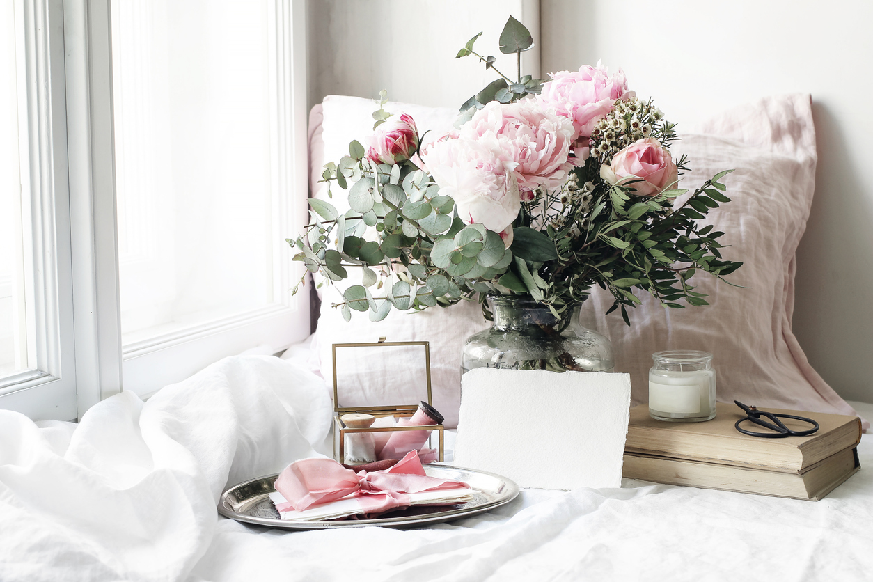 Spring, summer wedding still life scene. Blank paper card mockup, old books and linen pillow at windowsill. Vintage feminine floral composition, bouquet of pink roses, peony flowers and eucalyptus.