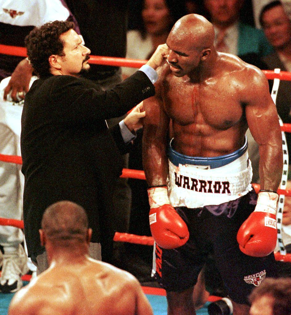 Blood flows down his arm and chest as Evander Holyfield (R) has his ear examined by the ringside doctor 28 June 1997 during his WBA heavyweight championship fight against Mike Tyson at the MGM Grand Garden Arena in Las Vegas, NV. Holyfield won by disqualification in the the third round after Tyson bit him.      AFP PHOTO/MIKE NELSON (Photo by MIKE NELSON / AFP)