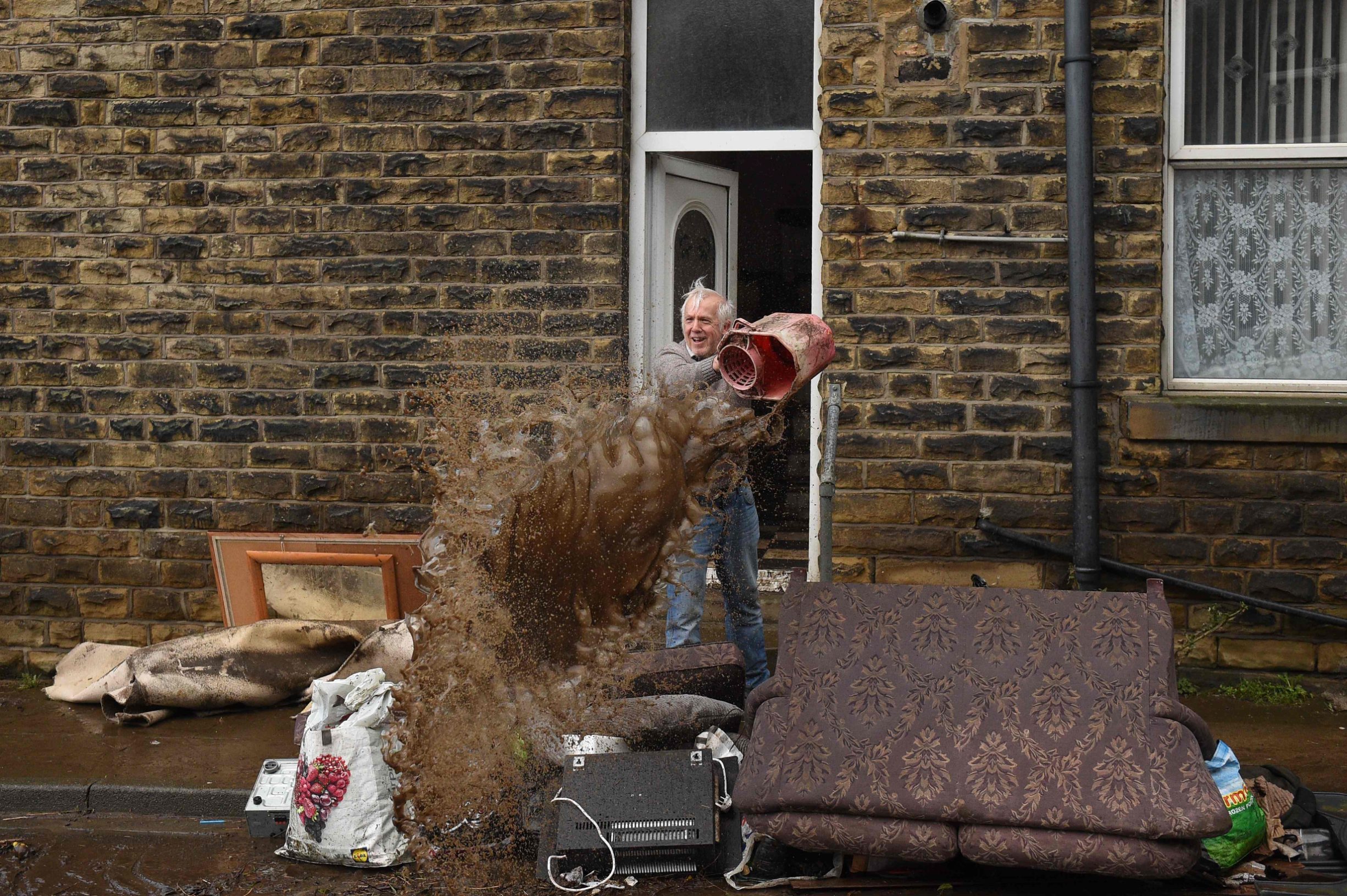 A man empties a bucket of water over debris outside a house in Mytholmroyd, northern England, on February 10, 2020 after flooding brought by Storm Ciara. - Storm Ciara grounded hundreds of flights Monday and left swatches of Europe without power after unleashing torrential rain and causing flash flooding that cancelled football matches in Britain. (Photo by Oli SCARFF / AFP)