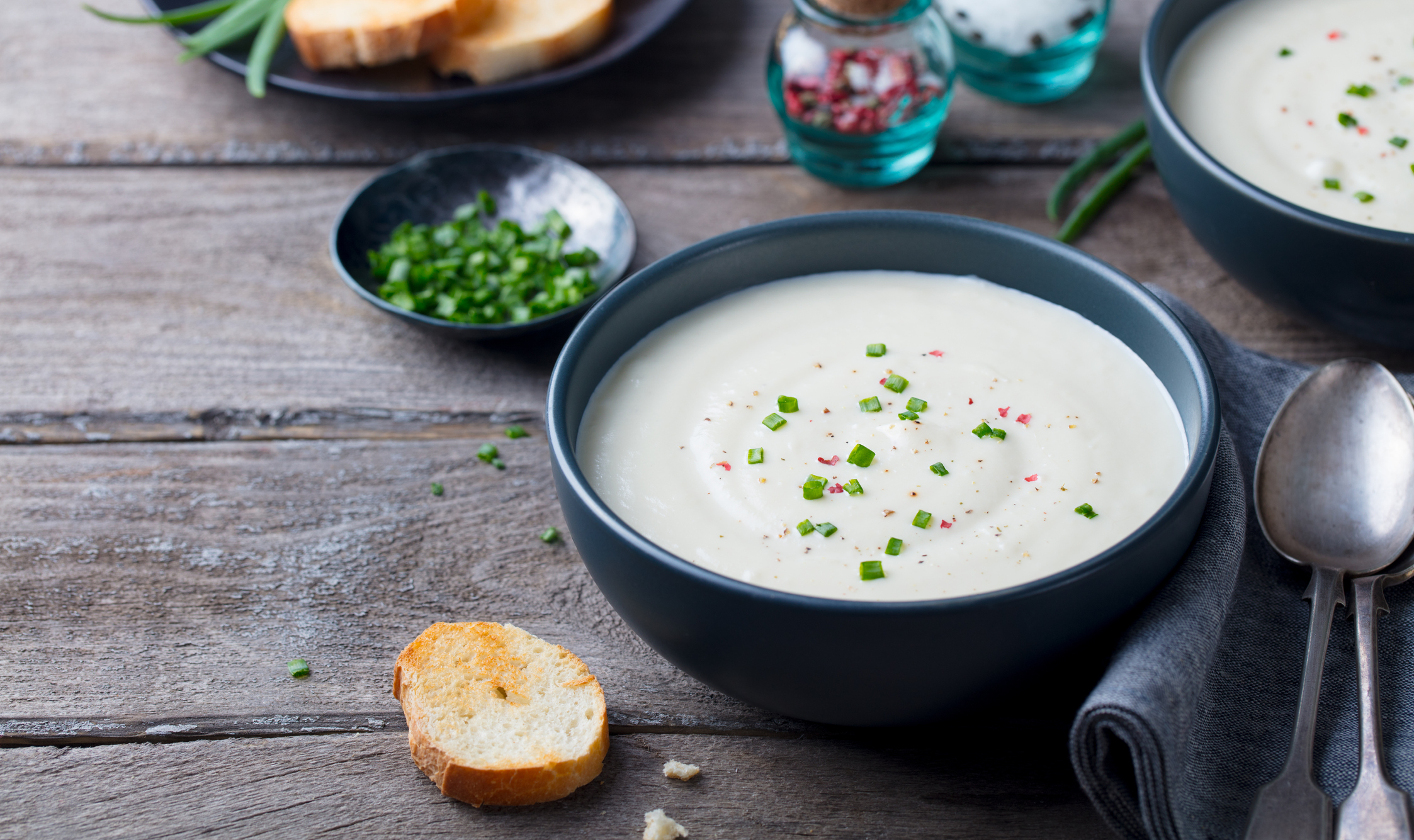 Cauliflower and potato cream soup with green onion in a bowl on grey wooden background. Copy space