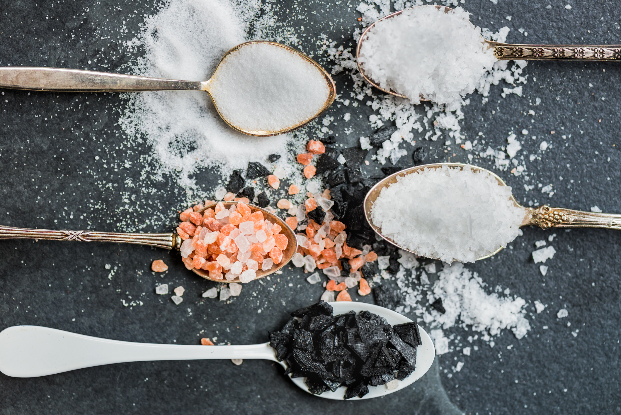 Different Kinds of Salt in Spoons, such as Himalayan Pink, Sea Original, Iodised Table, Sea Salt Flakes, Pink Diamonds, Black Sea Flakes, on Dark Background