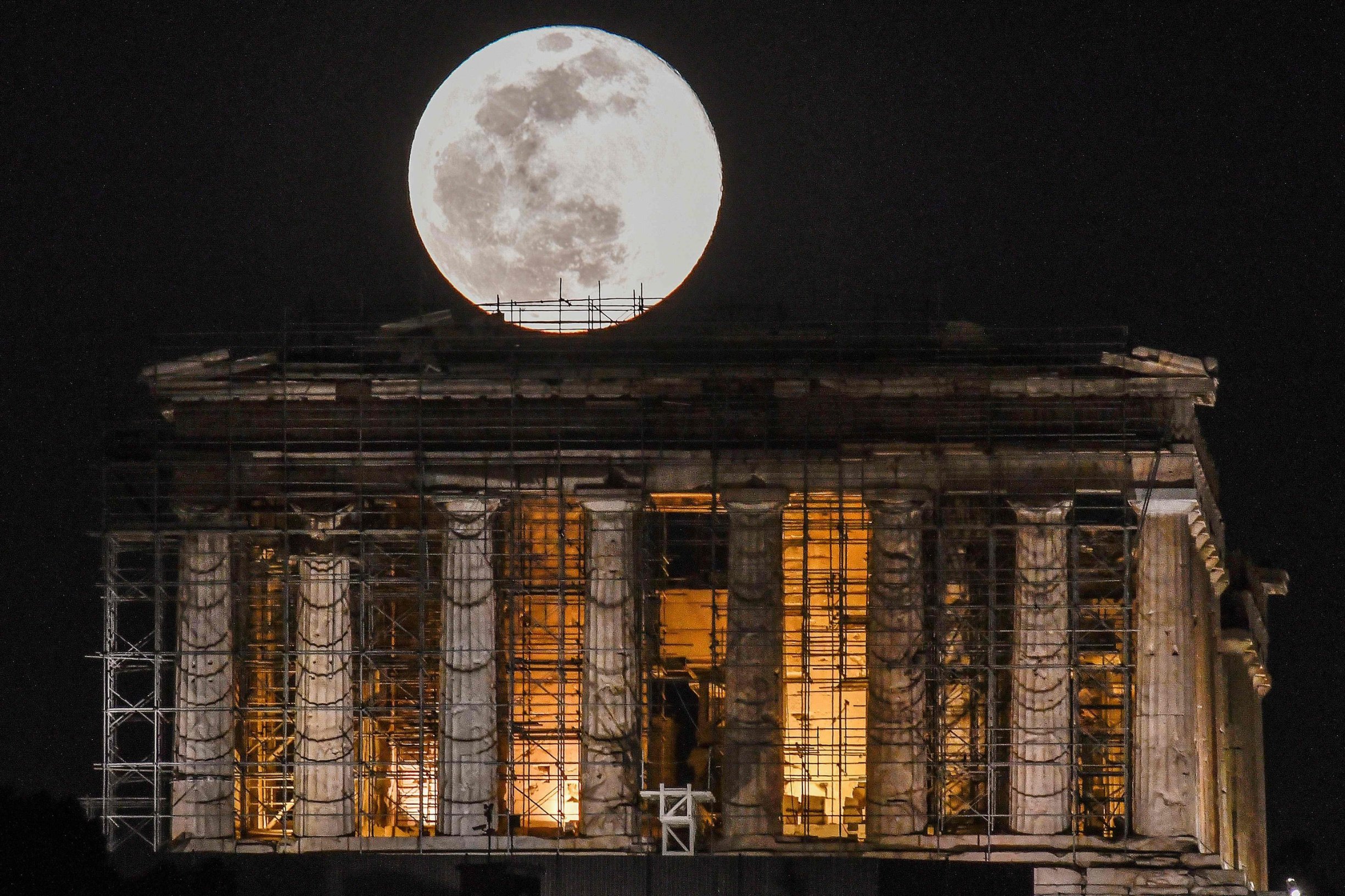 A full moon rises above Greek Parthenon Temple (438 BC), covered by scaffolding, at the Acropolis archaeological site in Athens on February 9, 2020 . (Photo by LOUISA GOULIAMAKI / AFP)