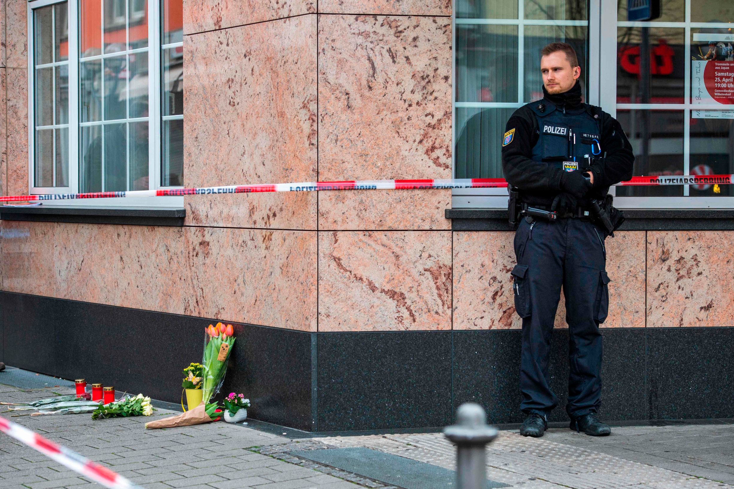 A police officer stands guard beside candles and flowers near one of the shooting targets, on February 20, 2020, at the Heumarkt in the centre of Hanau, near Frankfurt am Main, western Germany, after at least nine people were killed in two shootings late on February 19, 2020. - The suspect in two shootings in Germany that killed at least nine people was found dead at home, police said on February 20, 2020. At least nine people were killed in two shootings late on February 19 in Hanau, near the German city of Frankfurt. (Photo by Thomas Lohnes / AFP)