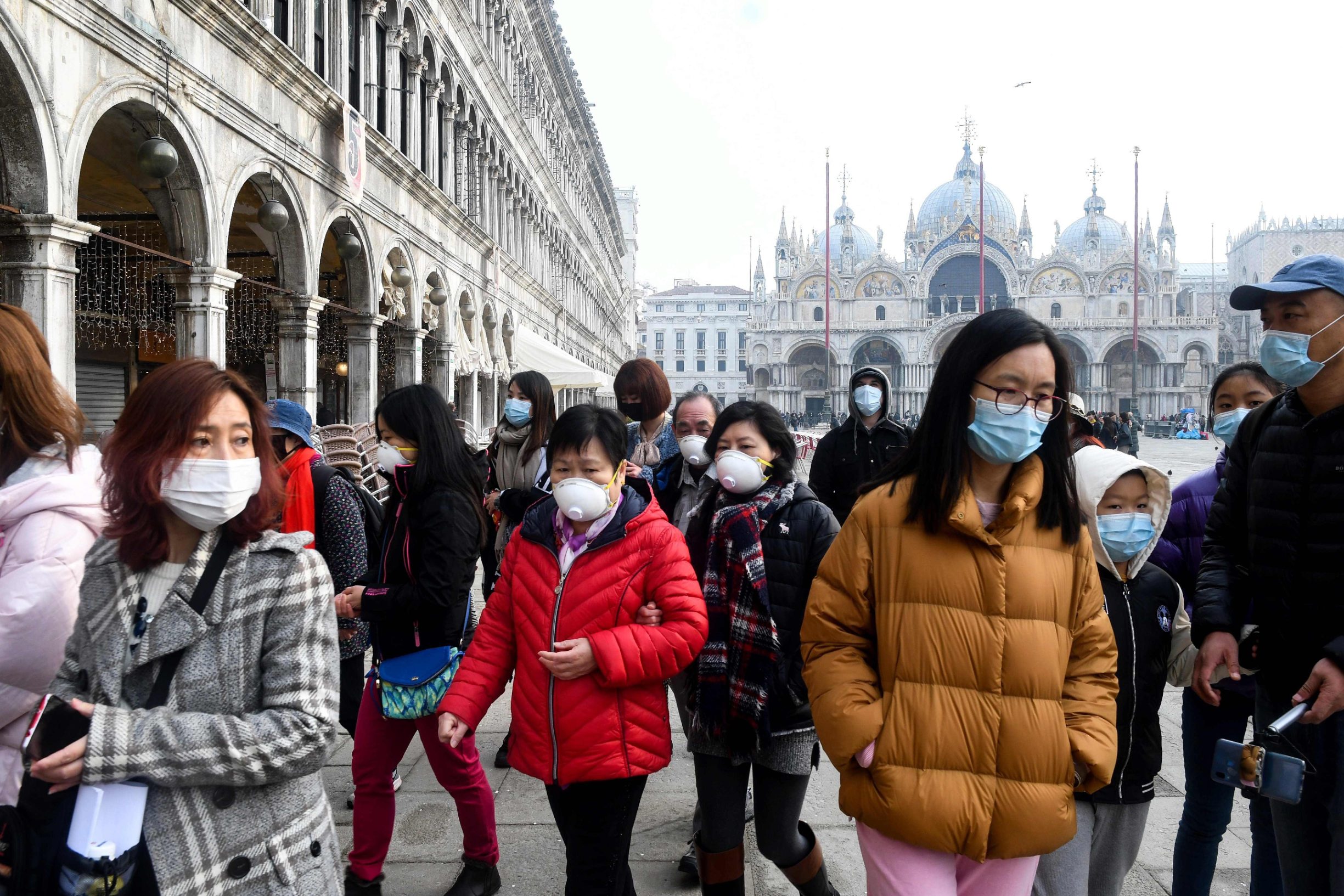 Tourists wearing protective facemasks visit the Piazza San Marco, in Venice, on February 24, 2020 during the usual period of the Carnival festivities which the last two days have been cancelled due to an outbreak of the COVID-19 the novel coronavirus, in northern Italy. - Italy reported on February 24, 2020 its fourth death from the new coronavirus, an 84-year old man in the northern Lombardy region, as the number of people contracting the virus continued to mount. (Photo by ANDREA PATTARO / AFP)