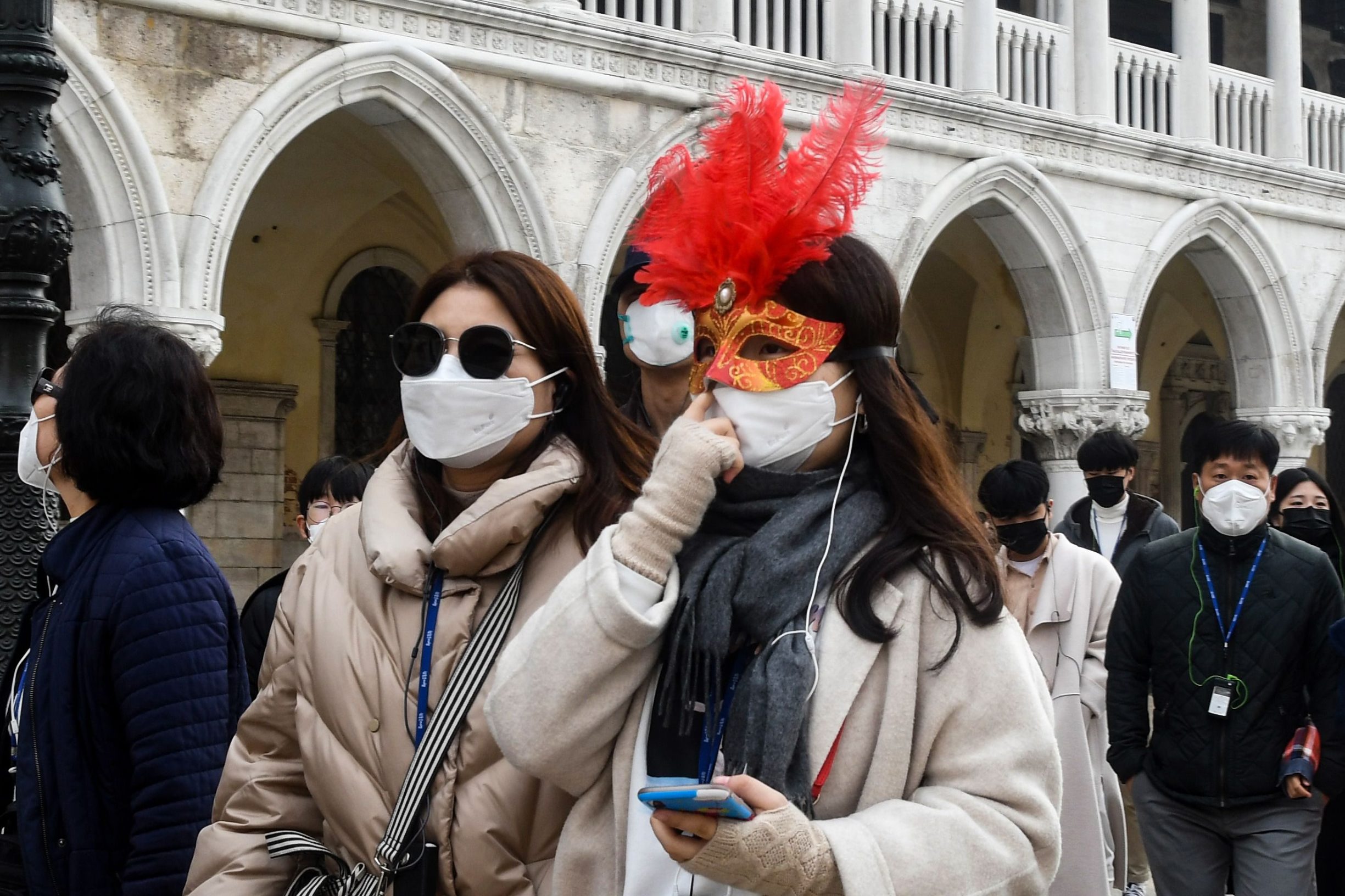 Tourists wearing protective facemasks and a Carnival mask visit the Piazza San Marco, in Venice, on February 24, 2020 during the usual period of the Carnival festivities which the last two days have been cancelled due to an outbreak of the COVID-19 the novel coronavirus, in northern Italy. - Italy reported on February 24, 2020 its fourth death from the new coronavirus, an 84-year old man in the northern Lombardy region, as the number of people contracting the virus continued to mount. (Photo by ANDREA PATTARO / AFP)