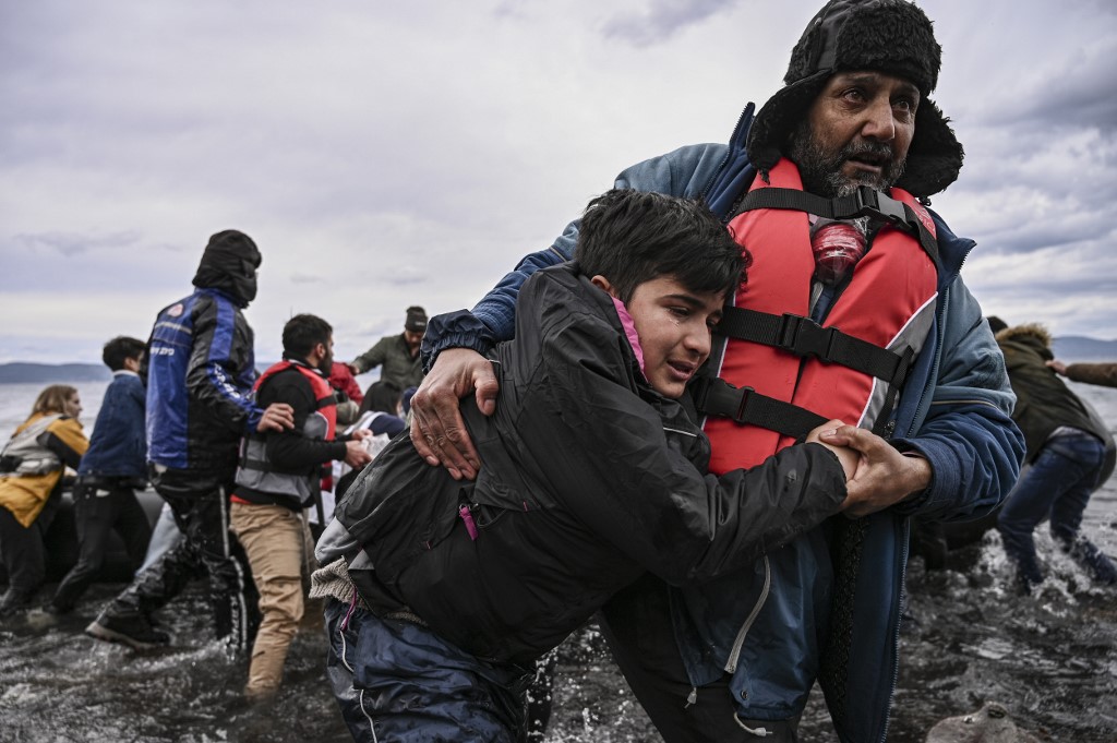 A man helps a young boy to walk after a dinghy with 54 Afghan refugees landed ashore the Greek island of Lesbos on February 28, 2020. - Turkey will no longer close its border gates to refugees who want to go to Europe, a senior official told AFP on February 28, shortly after the killing of 33 Turkish soldiers in an airstrike in northern Syria. (Photo by ARIS MESSINIS / AFP)
