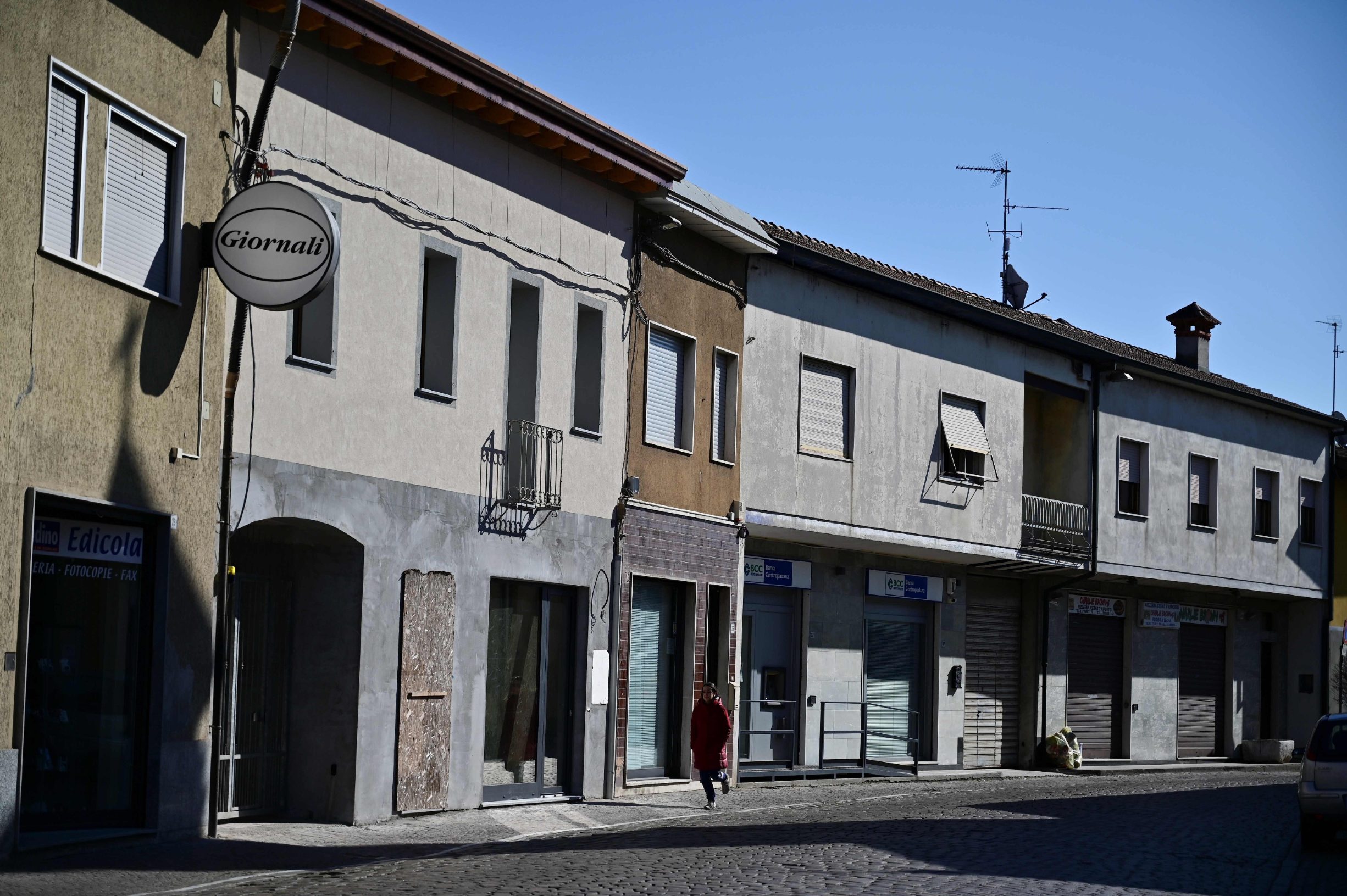 TOPSHOT - A woman walks past closed stores along the main street of Secugnano, the closest village to Zorlesco, southeast of Milan on February 26, 2020, which situated in the red zone of the COVID-19 the novel coronavirus outbreak in northern Italy. (Photo by MIGUEL MEDINA / AFP)