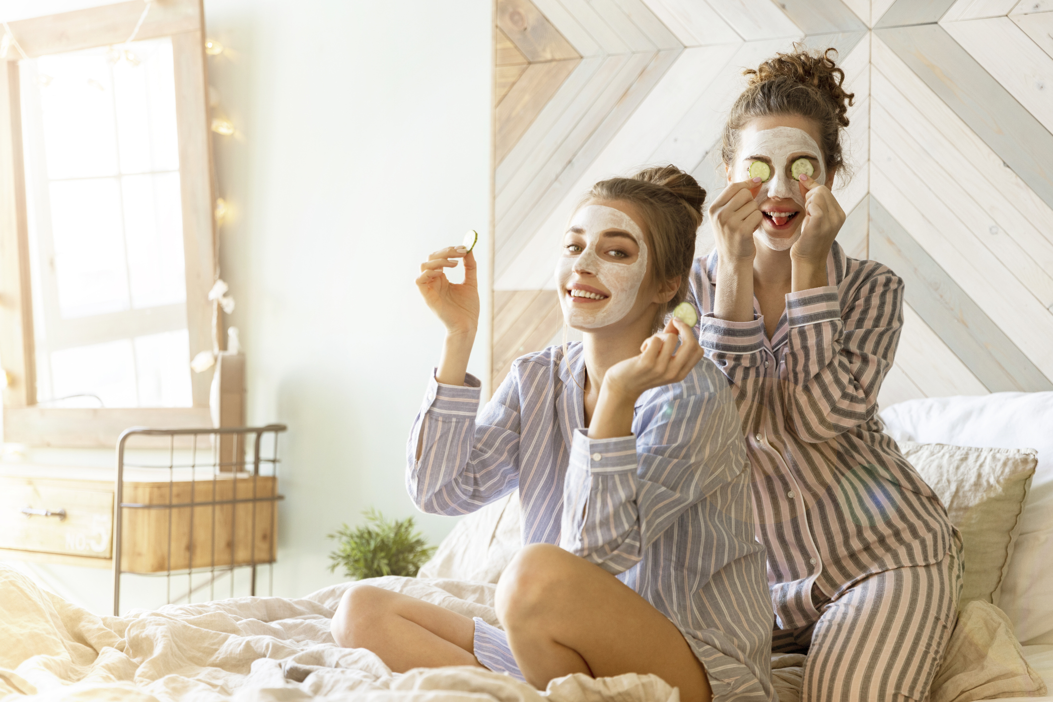 Portrait of blessed models in beauty-mask for face in comfortable bedroom. Beautifel women spending funny time together and posing for camera on bed. Blurred background