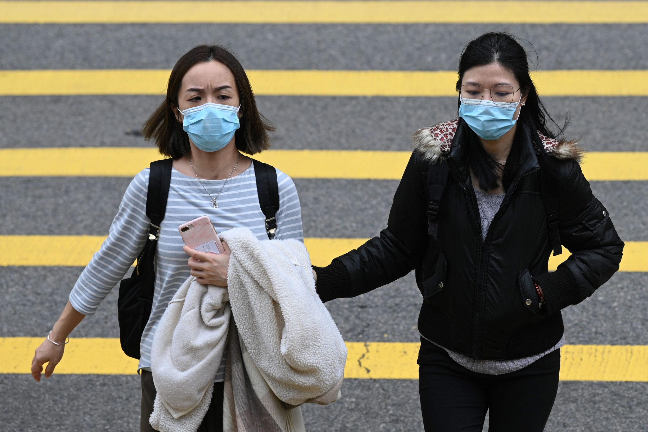 Two women wear face masks as they cross a road in Hong Kong on February 4, 2020, as a preventative measure following a virus outbreak which began in the Chinese city of Wuhan. - Hong Kong on February 4 become the second place outside of the Chinese mainland to report the death of a patient being treated for a new coronavirus that has so far claimed more than 400 lives. (Photo by Anthony WALLACE / AFP)