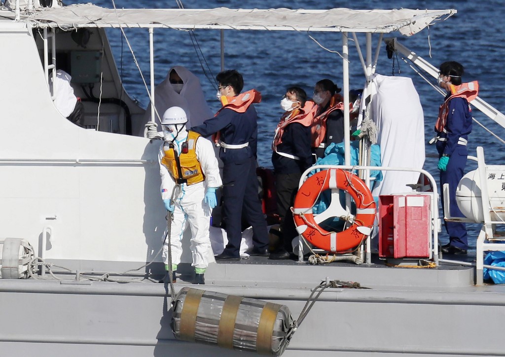 Workers in protective gear on board a Japan Coast Guard boat transfer a person wrapped in a white sheet (background L, in shadow) from the Diamond Princess cruise ship in Yokohama on February 5, 2020. - Thousands were marooned on a cruise ship off the Japanese coast, after medics evacuated 10 people infected with the deadly coronavirus, with many facing an anxious wait for their own test results. (Photo by STR / JIJI PRESS / AFP) / Japan OUT