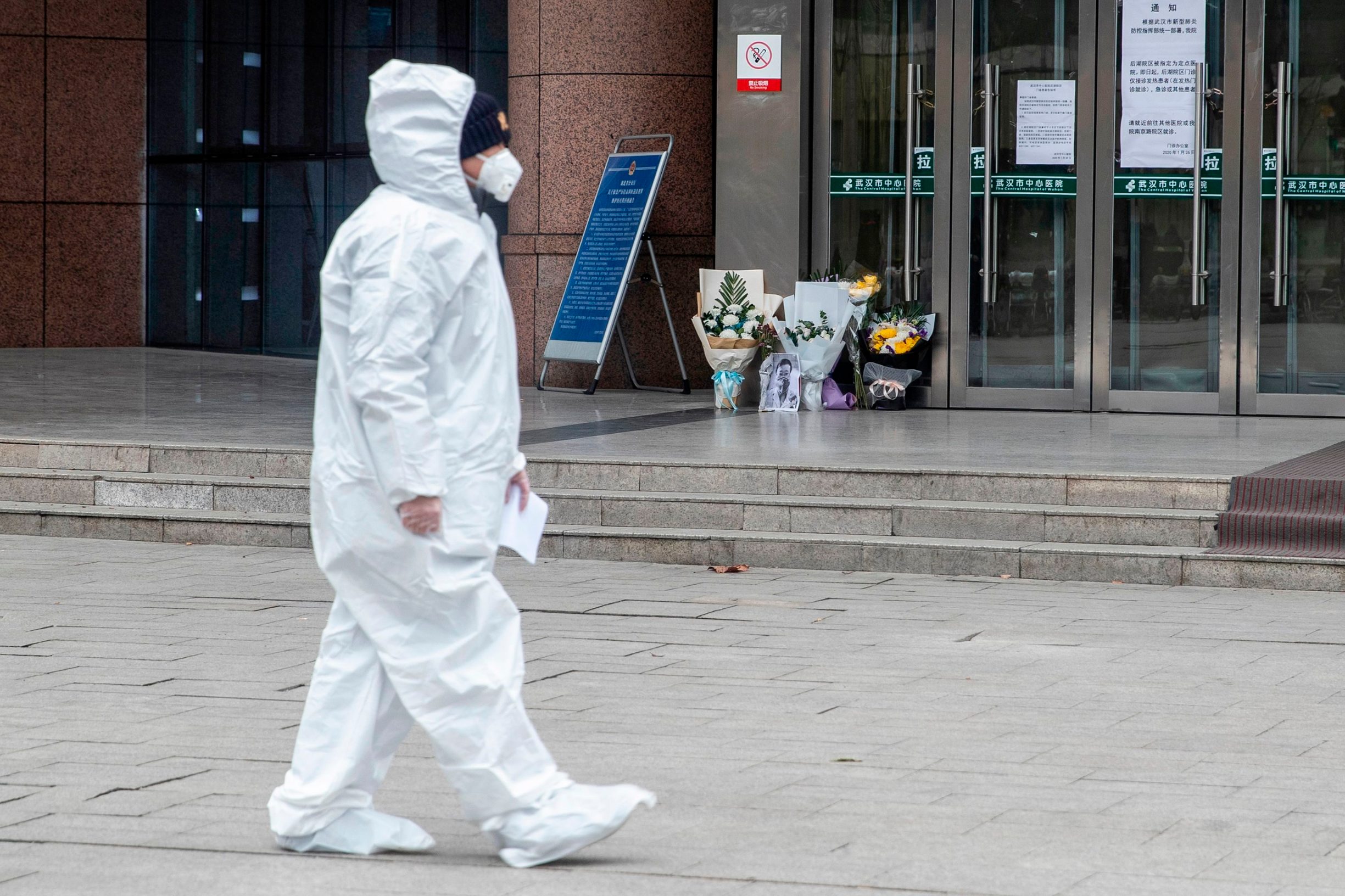 A medical staff member walks past a flower tribute to the late ophthalmologist Li Wenliang at the Houhu Branch of Wuhan Central Hospital in Wuhan in China's central Hubei province on February 7, 2020. - A Chinese doctor who was punished after raising the alarm about China's new coronavirus died from the pathogen on February 7, sparking an outpouring of grief and anger over a worsening crisis that has now killed more than 630 people. (Photo by STR / AFP) / China OUT