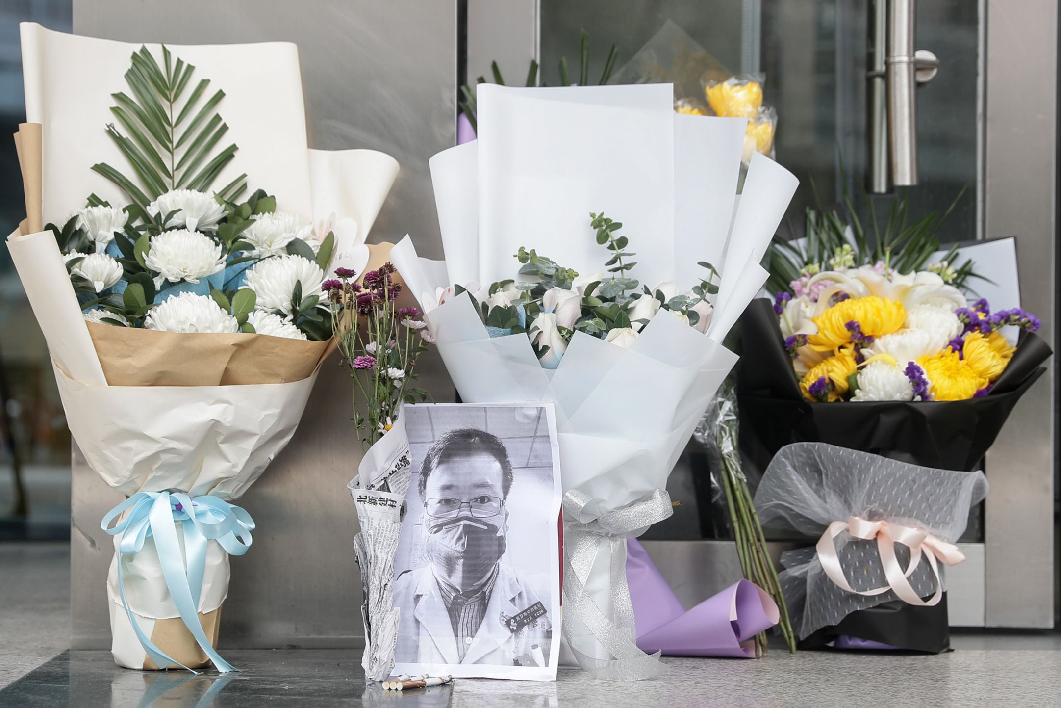 A photo of the late ophthalmologist Li Wenliang is seen with flower bouquets at the Houhu Branch of Wuhan Central Hospital in Wuhan in China's central Hubei province on February 7, 2020. - A Chinese doctor who was punished after raising the alarm about China's new coronavirus died from the pathogen on February 7, sparking an outpouring of grief and anger over a worsening crisis that has now killed more than 630 people. (Photo by STR / AFP) / China OUT