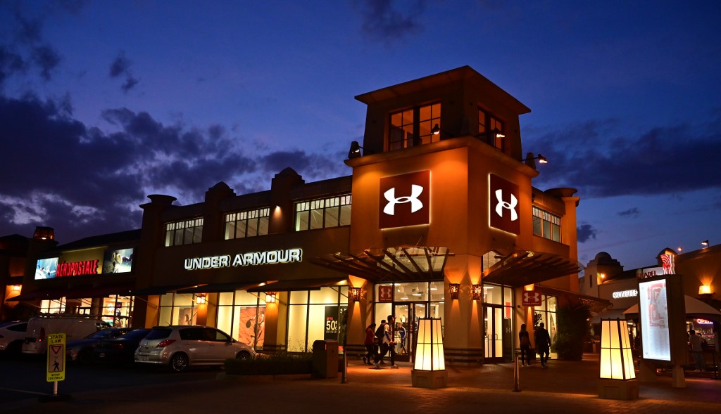 Shoppers walk past an Under Armour store at an outlet mall in Los Angeles on May 21, 2019. - More than 170 shoe companies and retailers, including Adidas, Nike, Skechers and Under Armour, have warned US President Donald Trump against a trade war with China, warning of the 