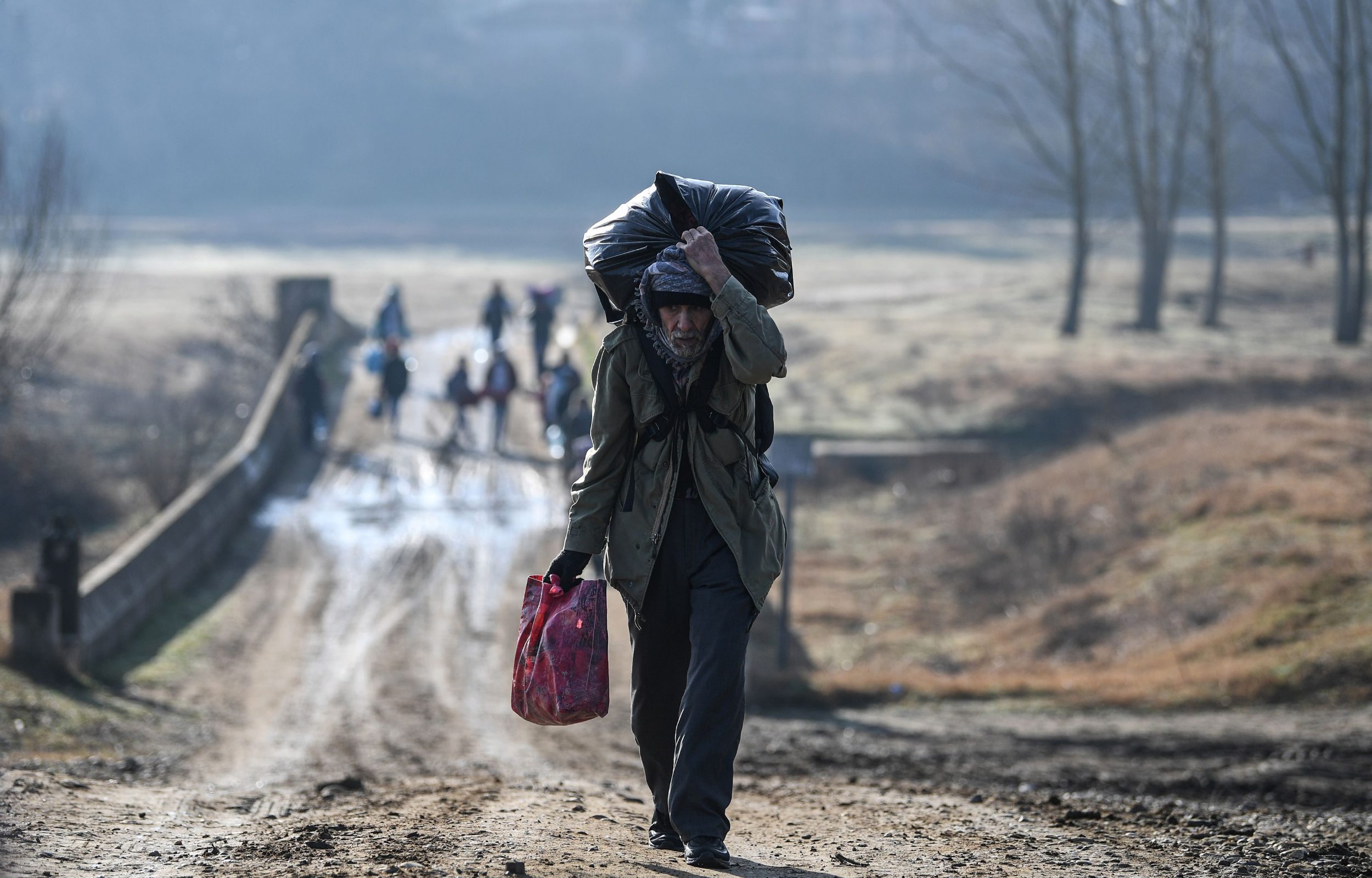 TOPSHOT - A migrant carries his belongings as he walks toward Meritsa river, near Edirne, to take a boat to attempt to enter Greece by crossing the river on March 1, 2020. - Thousands more migrants reached the Turkish border with Greece on March 1, 2020, AFP journalists said, after President threatened to let them cross into Europe. At least 2,000 people including women and children arrived on the morning from Istanbul and walked through a field towards the Pazarkule border gate, a correspondent said. The group included Afghans, Syrians and Iraqis. (Photo by Ozan KOSE / AFP)