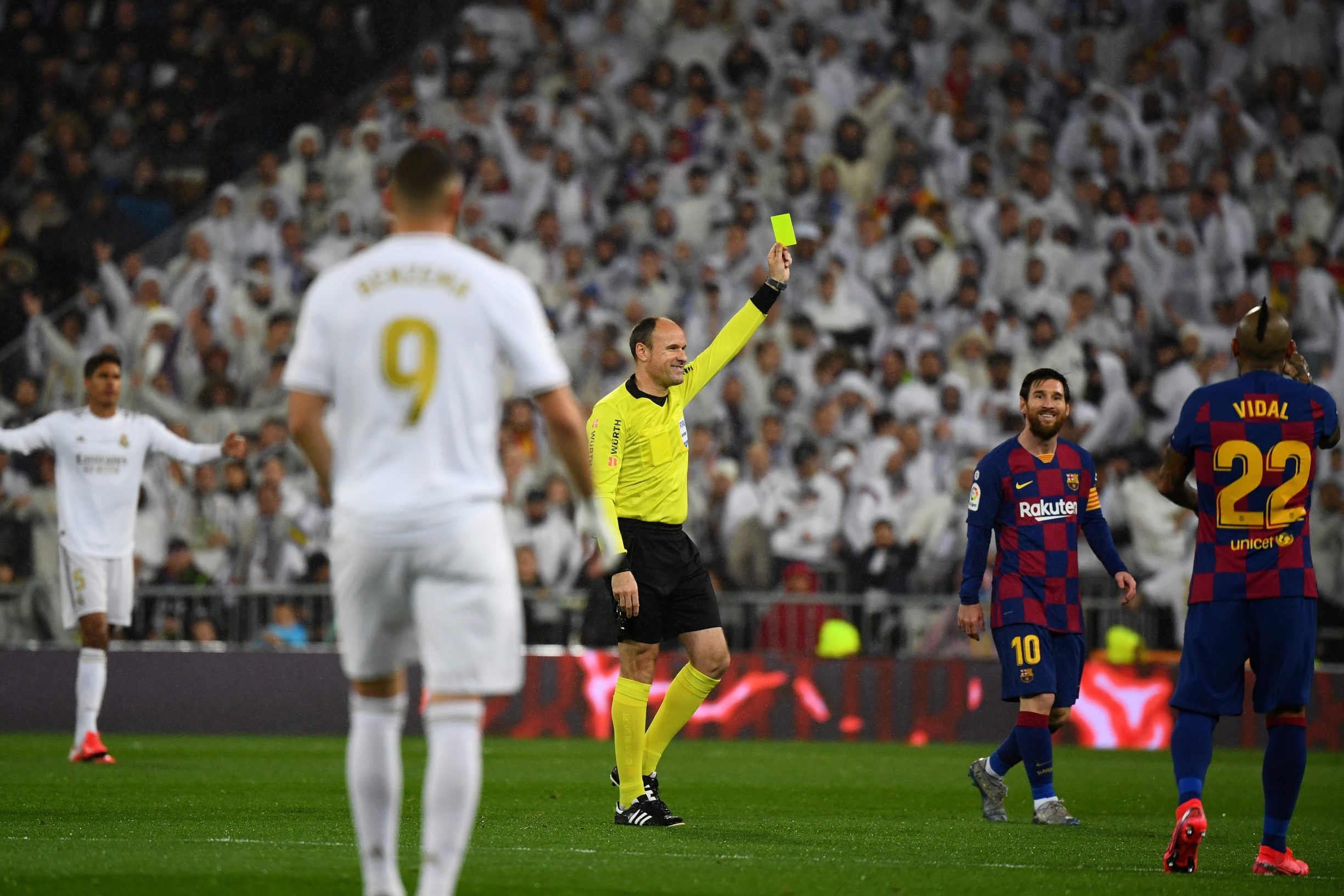 Barcelona's Argentine forward Lionel Messi (R) laughs as Spanish referee Antonio Miguel Mateu Lahoz (C) shows a yellow card to Real Madrid's Brazilian forward Vinicius Junior (not seen) during the Spanish League football match between Real Madrid and Barcelona at the Santiago Bernabeu stadium in Madrid on March 1, 2020. (Photo by GABRIEL BOUYS / AFP)
