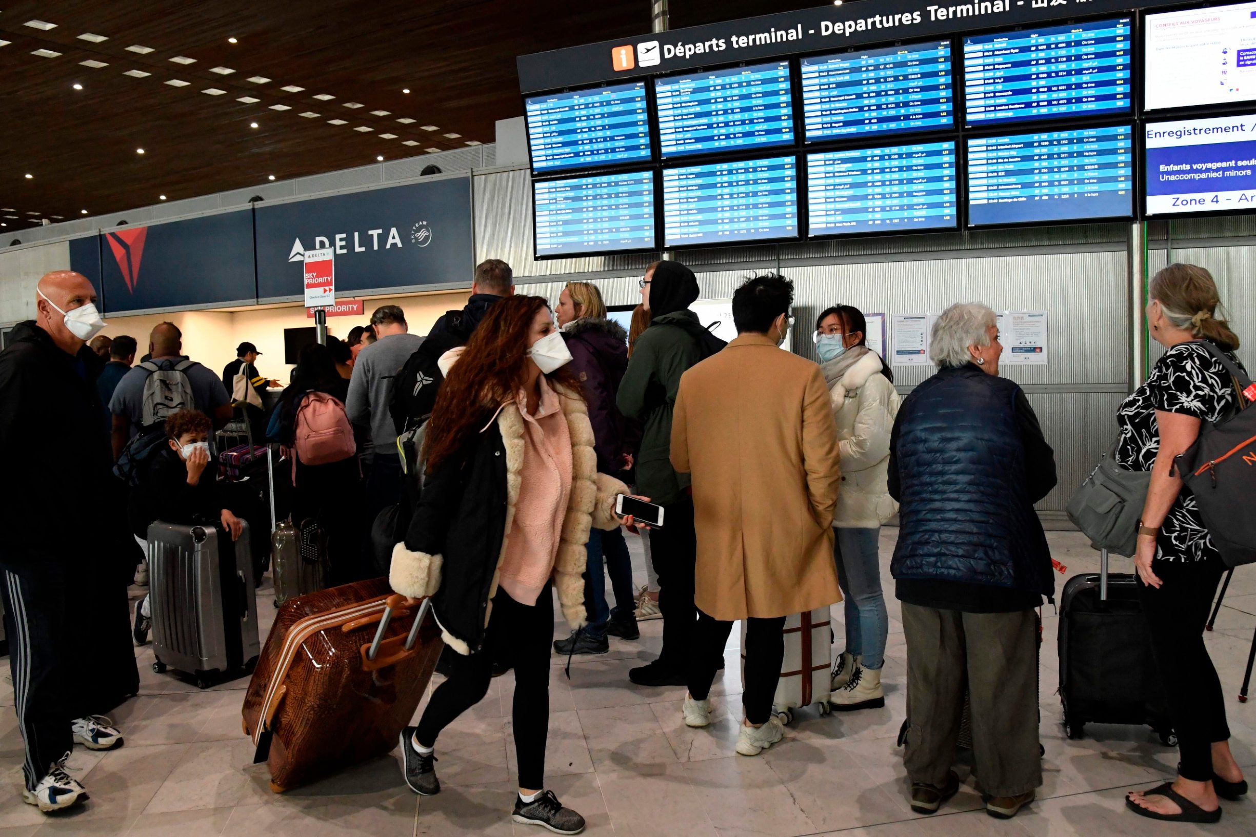 A traveller with a protective face mask pass by other standing in front of screens displaying departures flights at Paris-Charles-de-Gaulle airport after a US 30-day ban on travel from Europe due to the COVID-19 spread in Roissy-en-France on March 12, 2020. - US President Donald Trump announced on March 11, 2020 a shock 30-day ban on travel from mainland Europe over the coronavirus pandemic that has sparked unprecedented lockdowns, widespread panic and another financial market meltdown. (Photo by Bertrand GUAY / AFP)