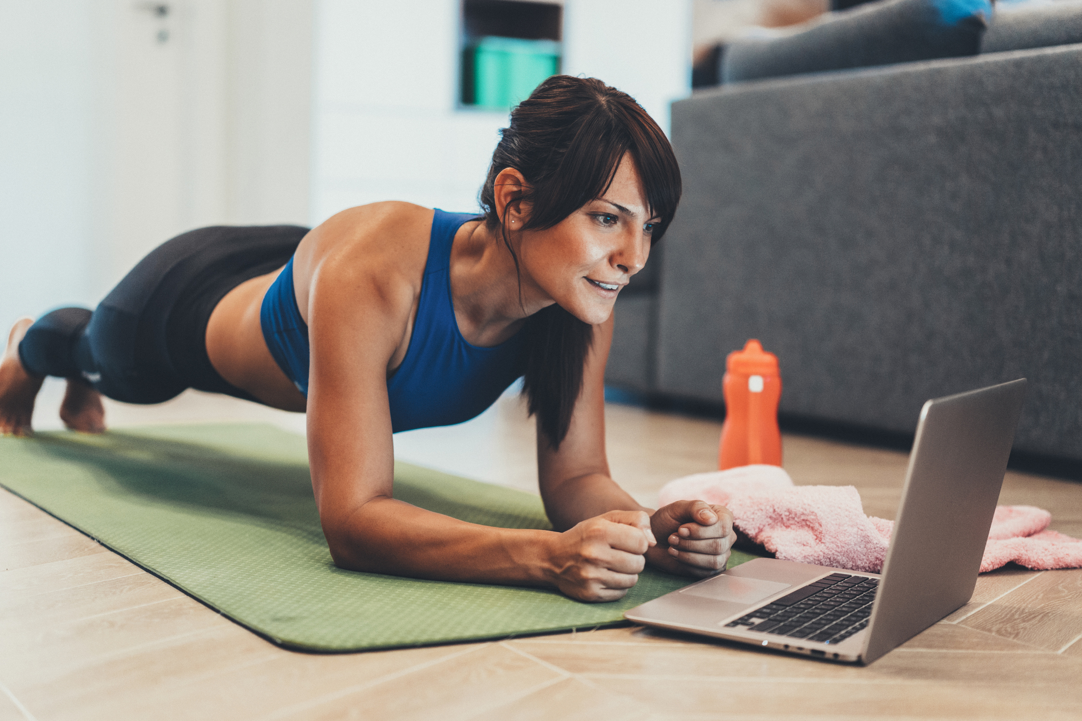 Strong sporty woman is doing working out at home and doing plank in front of her laptop