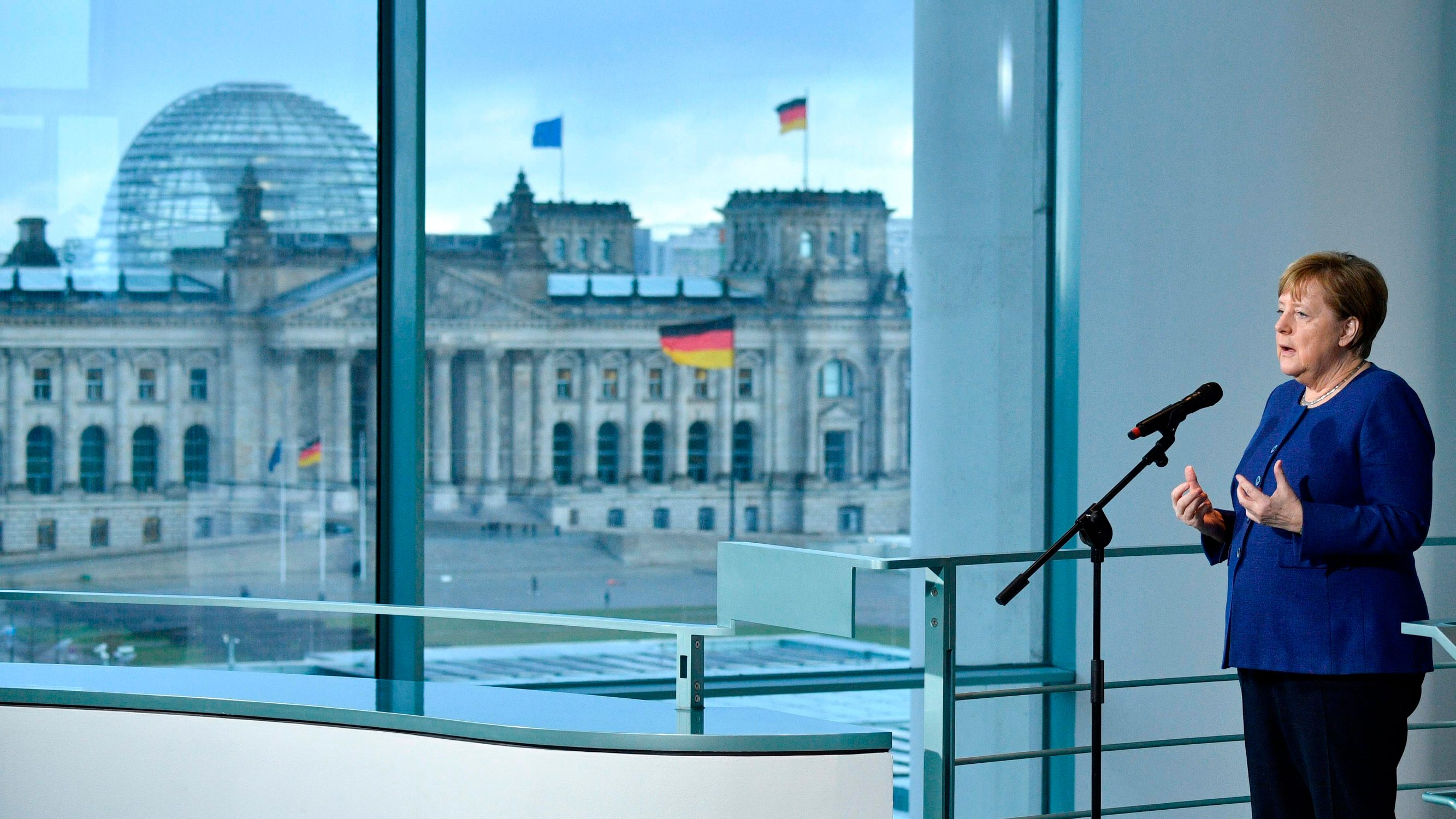 German Chancellor Angela Merkel makes a press statement before meeting with the heads of associations of the German economy and the trade unions  on the economic consequences of the spread of the coronavirus COVID-19 at the Chancellery, with a view of the Reichstag, the bukiding housing the lower house of parliament, through the window in Berlin on March 13, 2020. (Photo by John MACDOUGALL / POOL / AFP)