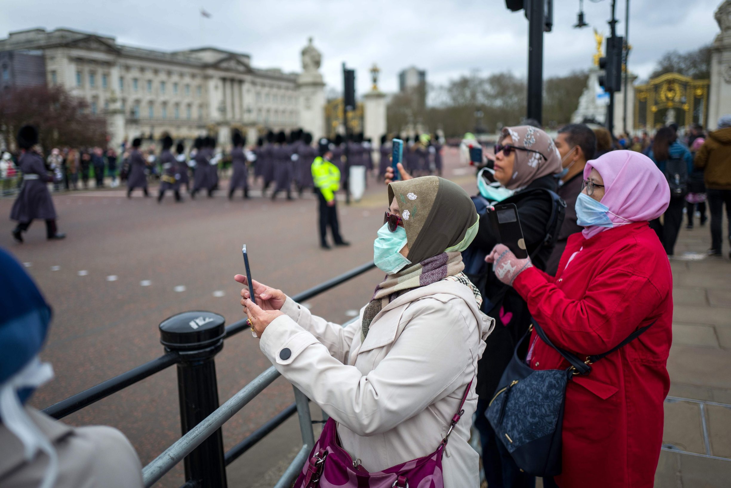 Tourists wearing protective face masks watch a changing of the Guards outside Buckingham Palace in London on March 15, 2020. (Photo by Tolga AKMEN / AFP)