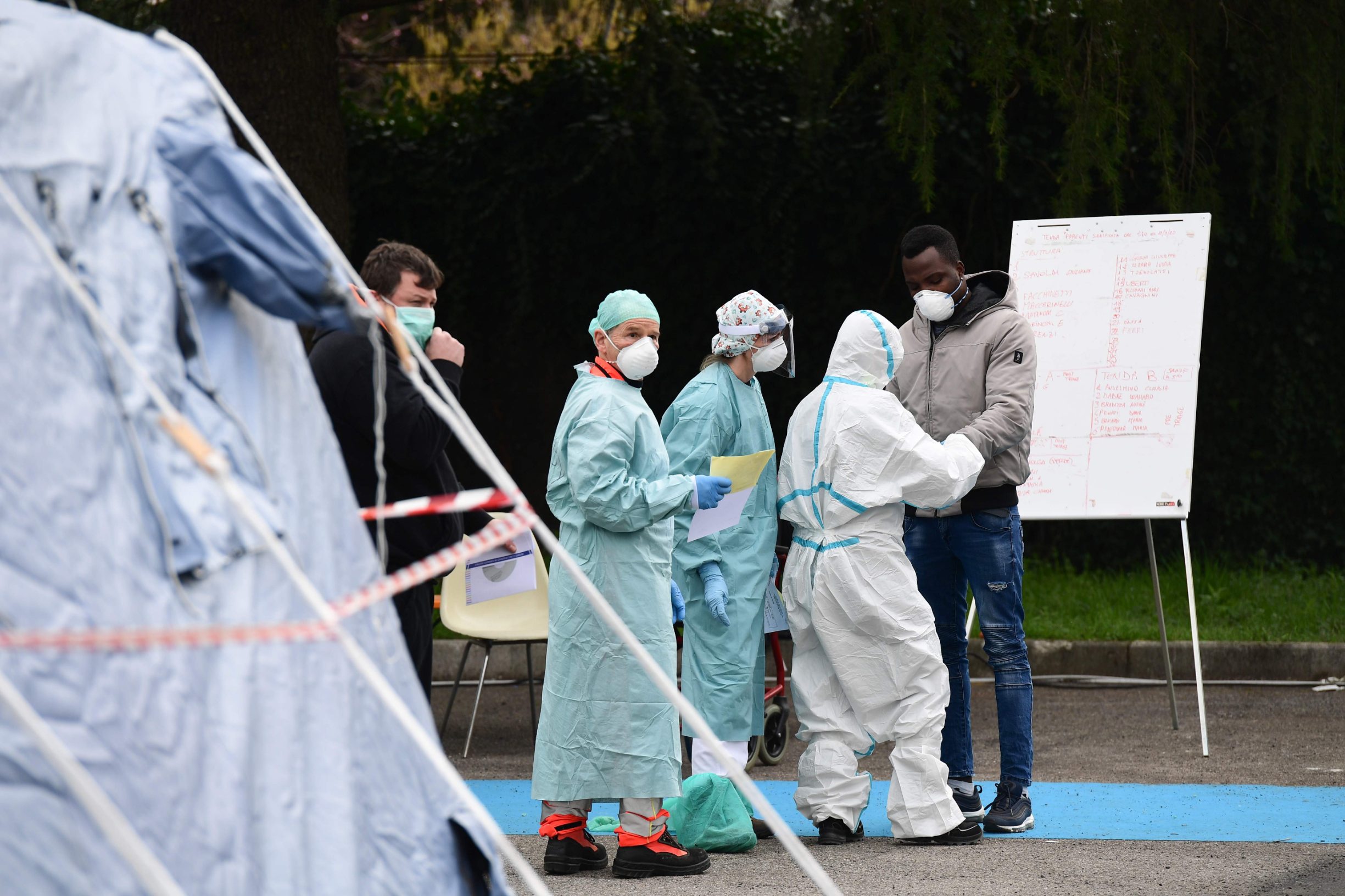 Hospital employees wearing a protection mask and gear tend to a patient (R) coming in to be tested at a temporary emergency structure set up outside the accident and emergency department, where any new arrivals presenting suspect new coronavirus symptoms are being tested, at the Brescia hospital, Lombardy, on March 13, 2020. (Photo by Miguel MEDINA / AFP)