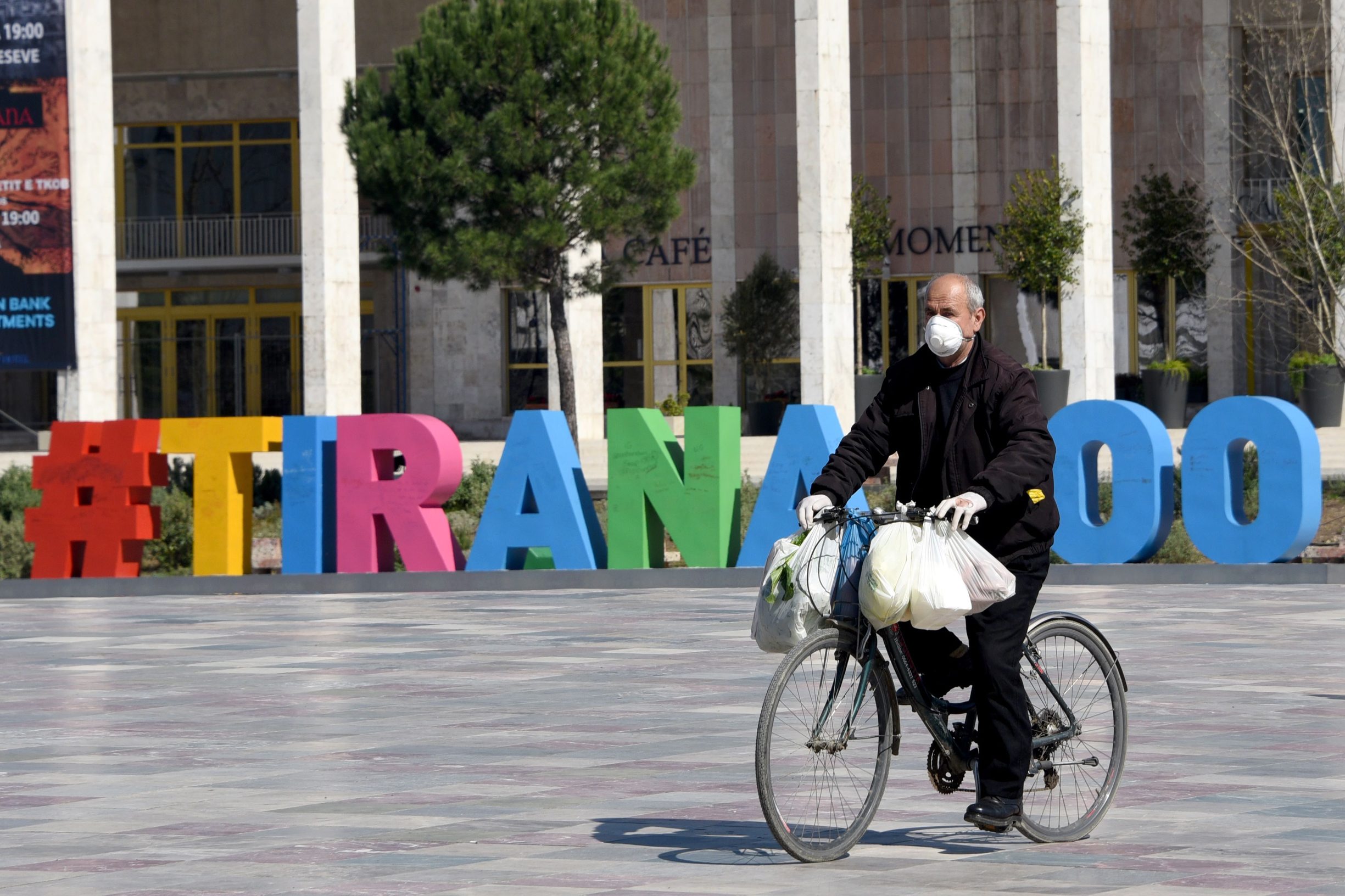 A man wearing protective mask rides his bicycle in Tirana's main square on March 12, 2020. - Albania has banned the circulation of all cars (except ambulances and supplies) for 3 days as it adds on more restrictive measures to prevent the spread of the coronavirus after the number of infected people raised to 23. Hefty fines of the euro 5000 have been imposed for those found breaching the rules. (Photo by Gent SHKULLAKU / AFP)