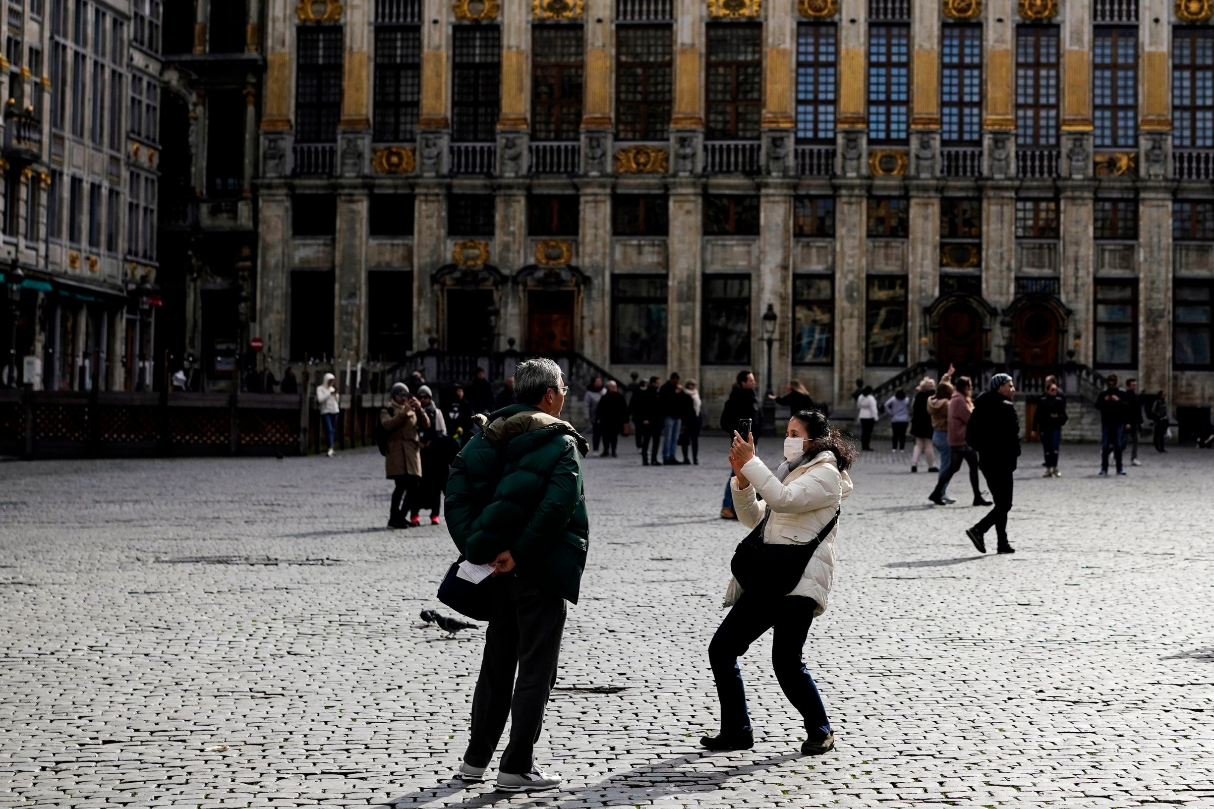 A tourist wears a protective face mask as she takes a picture with her mobile phone at the Grand-Place in the centre of Brussels, amid the outbreak of COVID-19, caused by the novel coronavirus. - Belgium close schools, cancel all cultural events and shutter bars and restaurants to stave off the spread of the coronavirus outbreak.  Beginning on March 14, only stores that provide essential services -- such as pharmacies and grocery stores-- will remain open under normal conditions. (Photo by Kenzo TRIBOUILLARD / AFP)
