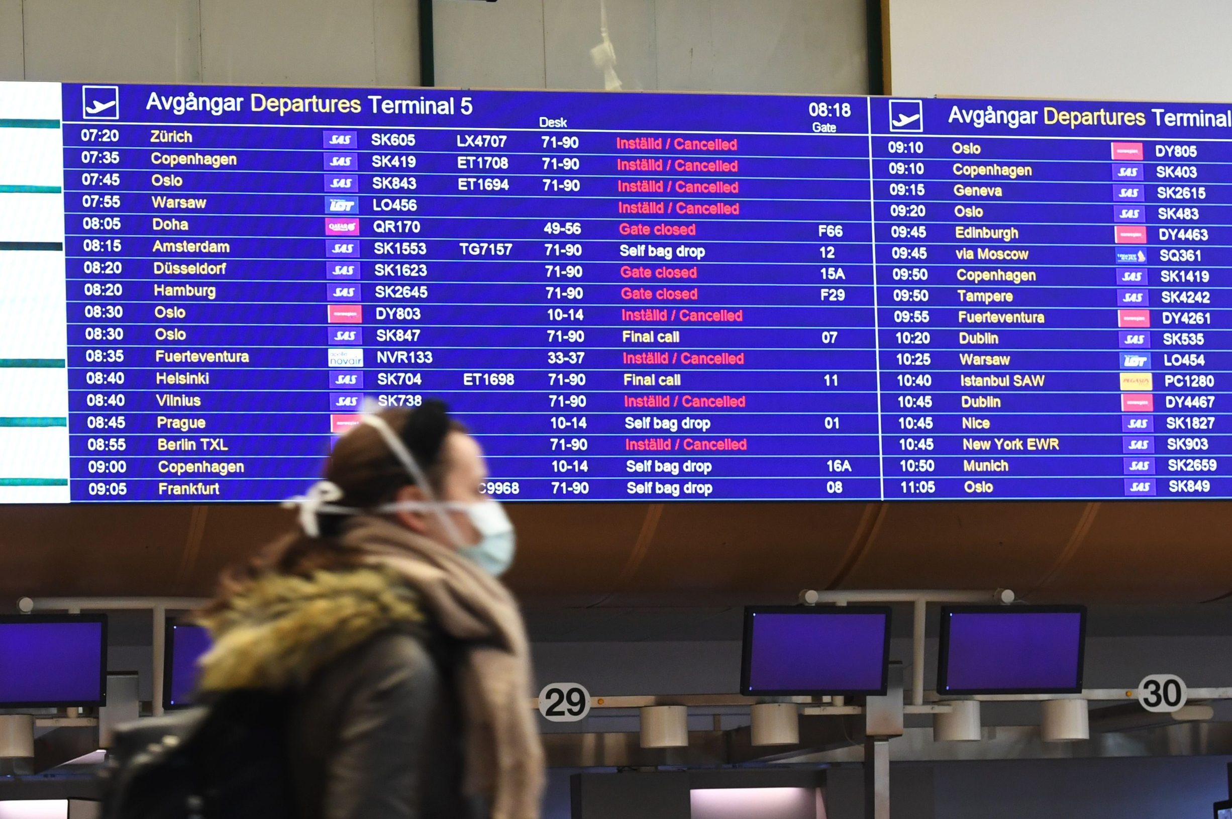 A passenger walks past an information board announcing flight cancellations at Arlanda international airport outside Stockholm, with the airport being unusually empty due to concerns over the spread of the novel coronavirus on March 16, 2020. (Photo by Fredrik SANDBERG / TT NEWS AGENCY / AFP) / Sweden OUT