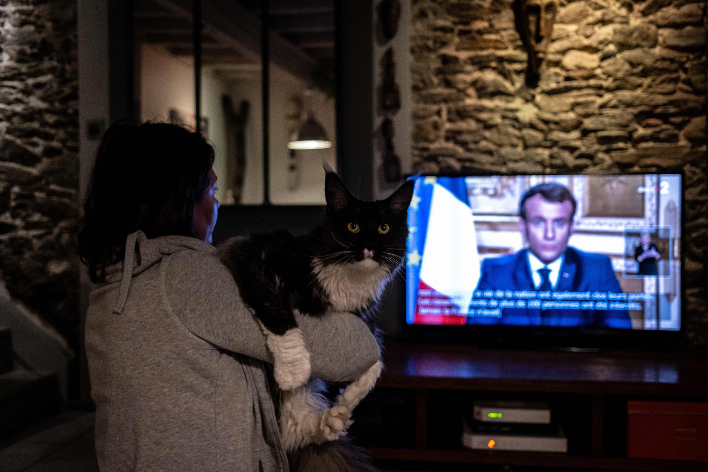 A person holds a catch while watching Frrench President Emmanuel Macron in Givors near Lyon, as he speaks from Paris during a televised address to the nation on the outbreak of COVID-19, caused by the novel coronavirus, on March 16, 2020. - The French president addresses the nation, with many expecting him to unveil more strict home confinement rules in a bid to prevent the virus from spreading. France has closed down all schools, theatres, cinemas and a range of shops, with only those selling food and other essential items allowed to remain open. The balance sheet of the epidemic climbed to 127 dead and 5,423 confirmed cases in France. (Photo by JEAN-PHILIPPE KSIAZEK / AFP)
