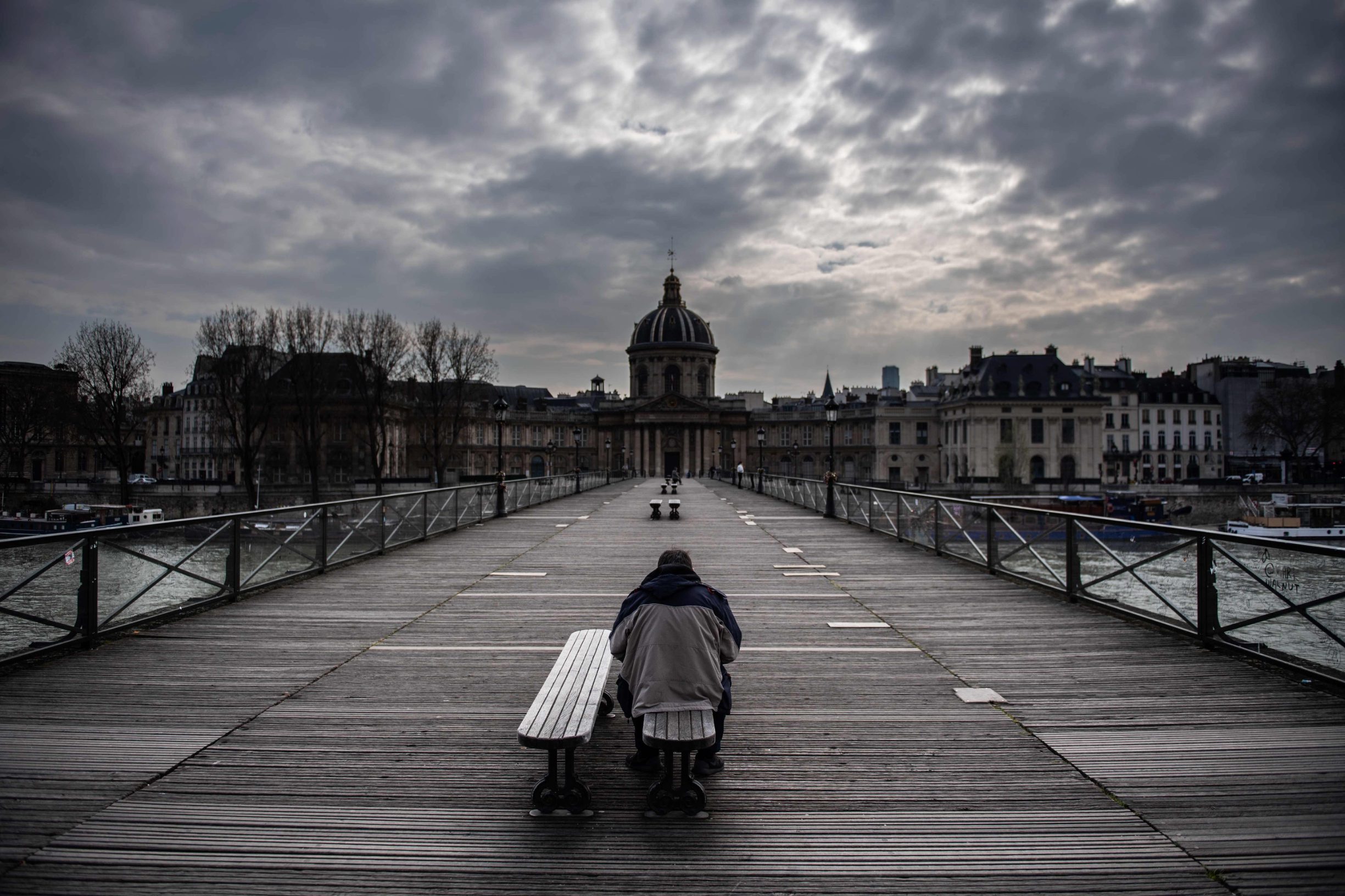 A man waits on a bench of the Pont Des Arts in Paris on March 17, 2020 as a strick lockdown comes into in effect to stop the spreading of the COVID-19 in the country. - French President asked people to stay at home to avoid the spreading the Covid-19, saying only necessary trips would be allowed and violations would be punished. The country has already shut cafes, restaurants, schools and universities and urged people to limit their movements. (Photo by Martin BUREAU / AFP)