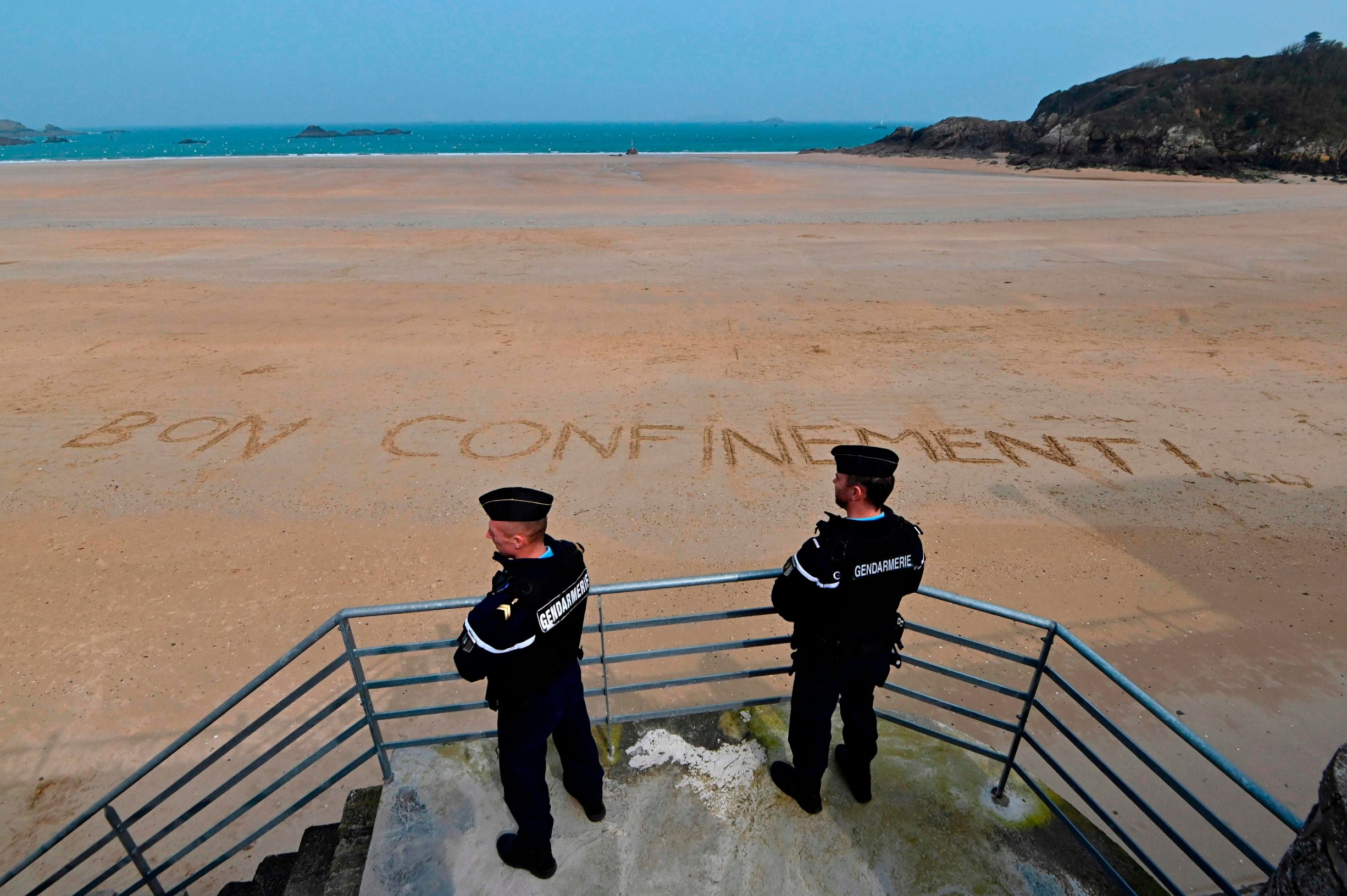 French gendarmes patrol on an empty beach with a message written on the sand, reading 'nice confinement' on March 20, 2020 in the western city of Saint-Lunaire,  on the fourth day of a strict lockdown in France to stop the spread of the novel coronavirus (COVID-19). (Photo by Damien Meyer / AFP)