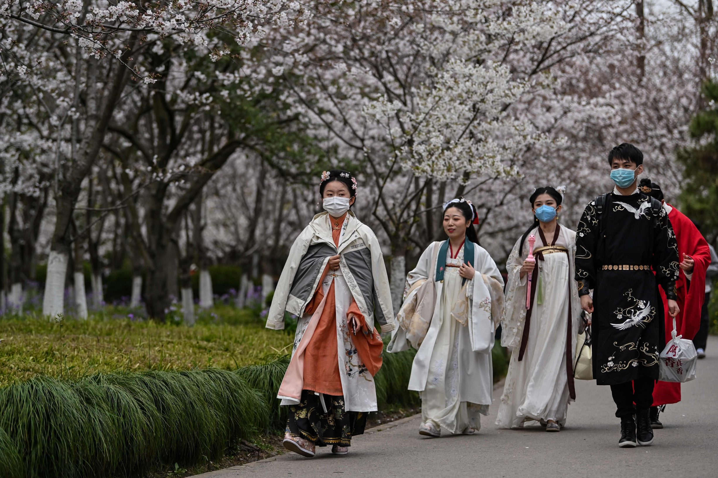 Young people wearing facemasks amid concerns over the spread of the COVID-19 novel coronavirus, walk dressed in Tang Dynasty costumes at Century Park in Shanghai on March 22, 2020. (Photo by Hector RETAMAL / AFP)