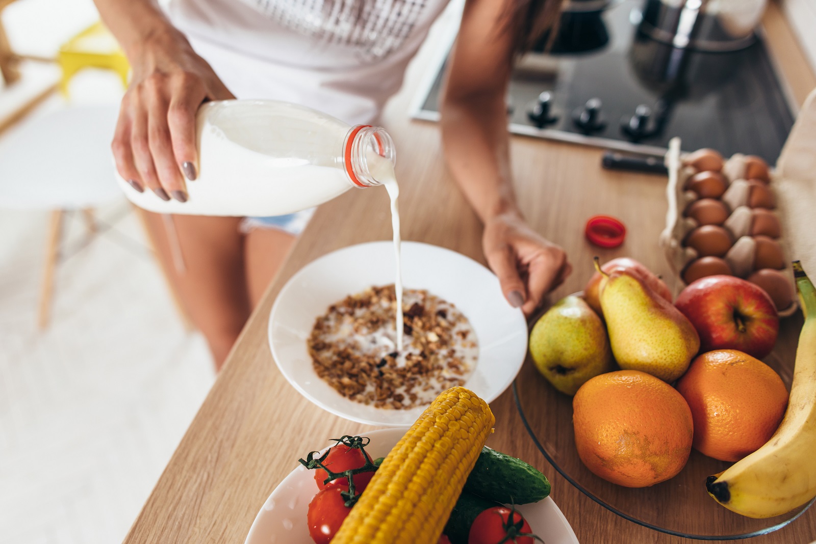 Woman pours milk into a bowl. Muesli fruits vegetables