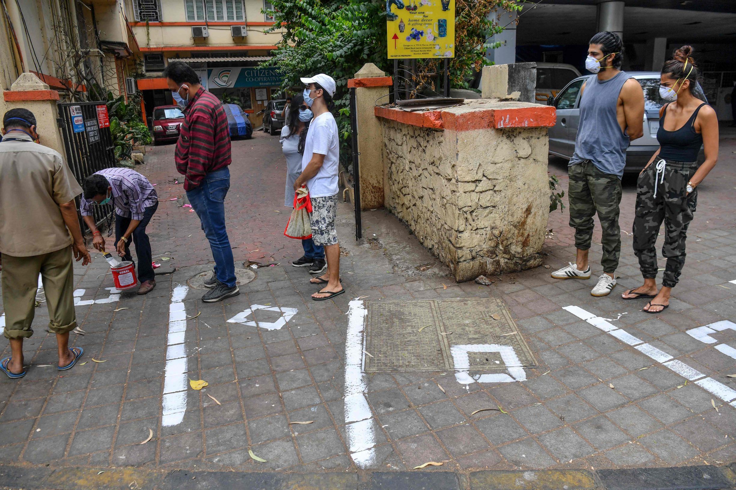 Customers watch municipal workers (L) painting white marks on the floor to help maintaining recommended social distanciation as they queue outside a departmental store during a government-imposed nationwide lockdown as a preventive measure against the COVID-19 coronavirus in Mumbai on March 26, 2020. (Photo by INDRANIL MUKHERJEE / AFP)