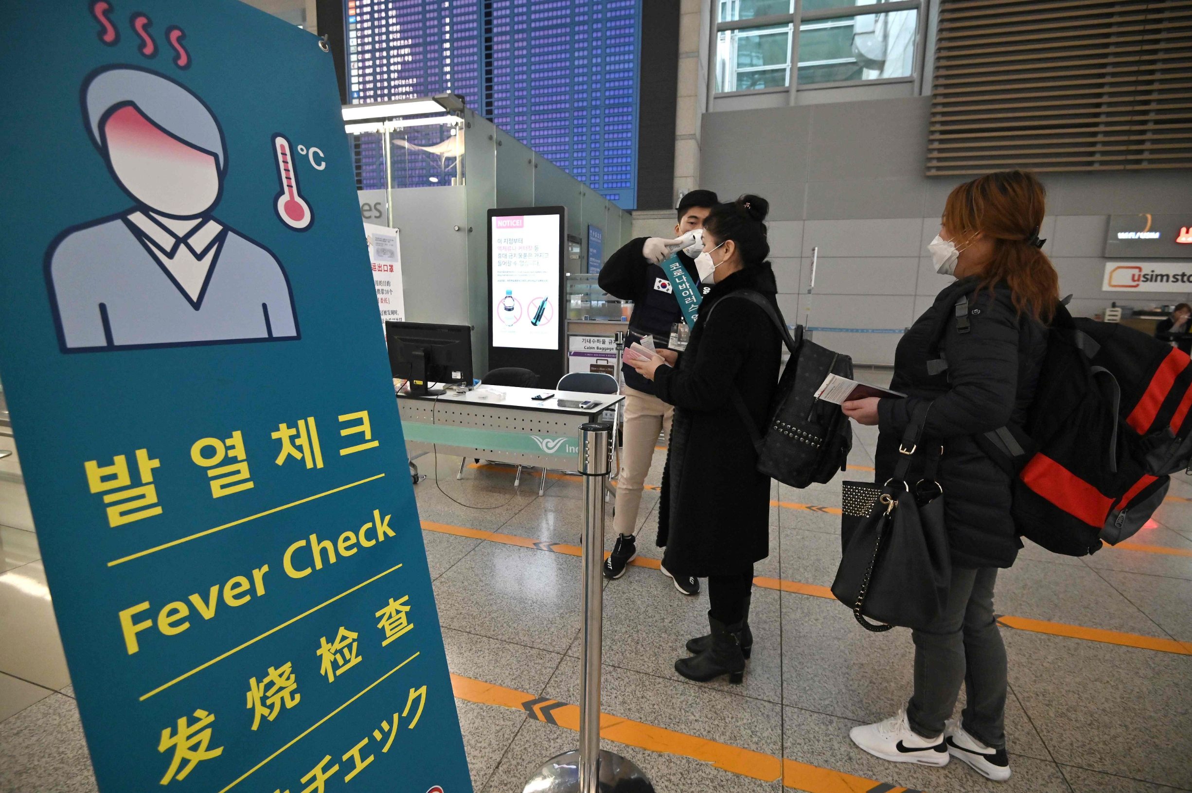 A member of the South Korean military support team (L) checks the body temperature of a passenger at a gate in the departure hall at Incheon international airport, west of Seoul, on March 17, 2020. - Airlines have cancelled so many routes as scores of countries have imposed bans or restrictions on arrivals from South Korea amid concerns over the COVID-19 coronavirus outbreak. (Photo by Jung Yeon-je / AFP)