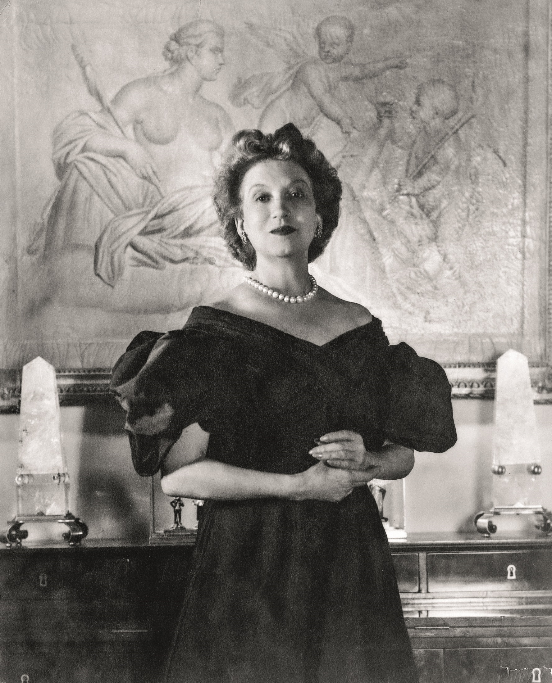 Portrait of Canadian-born beautician and cosmetics entrepreneur Elizabeth Arden (1878 - 1966) dressed in a ball gown as she clasps her hands together and stands in front of a framed piece of art, 1947. (Photo by Hulton Archive/Getty Images) 